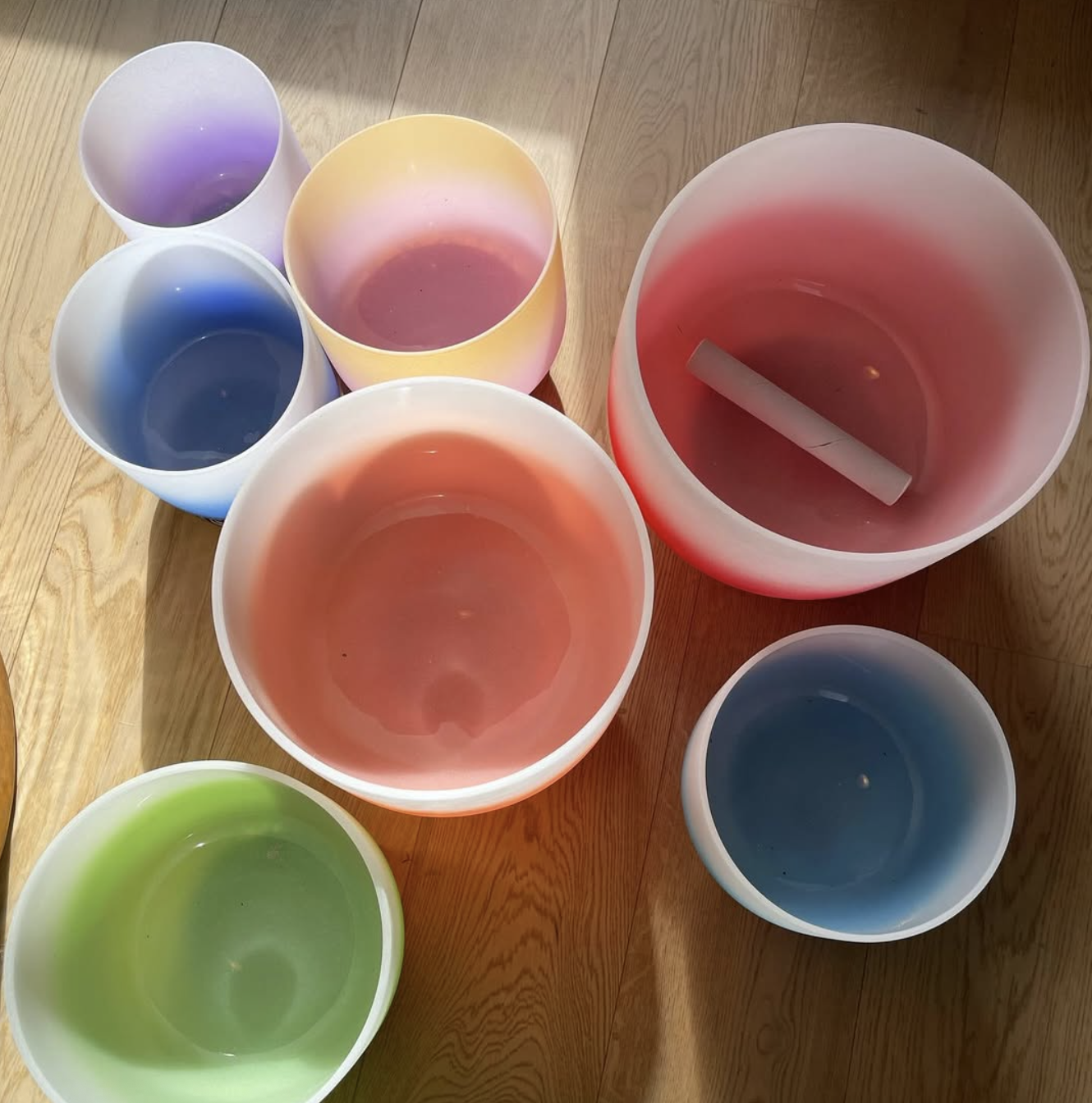 Colorful singing bowls arranged on a wooden floor.