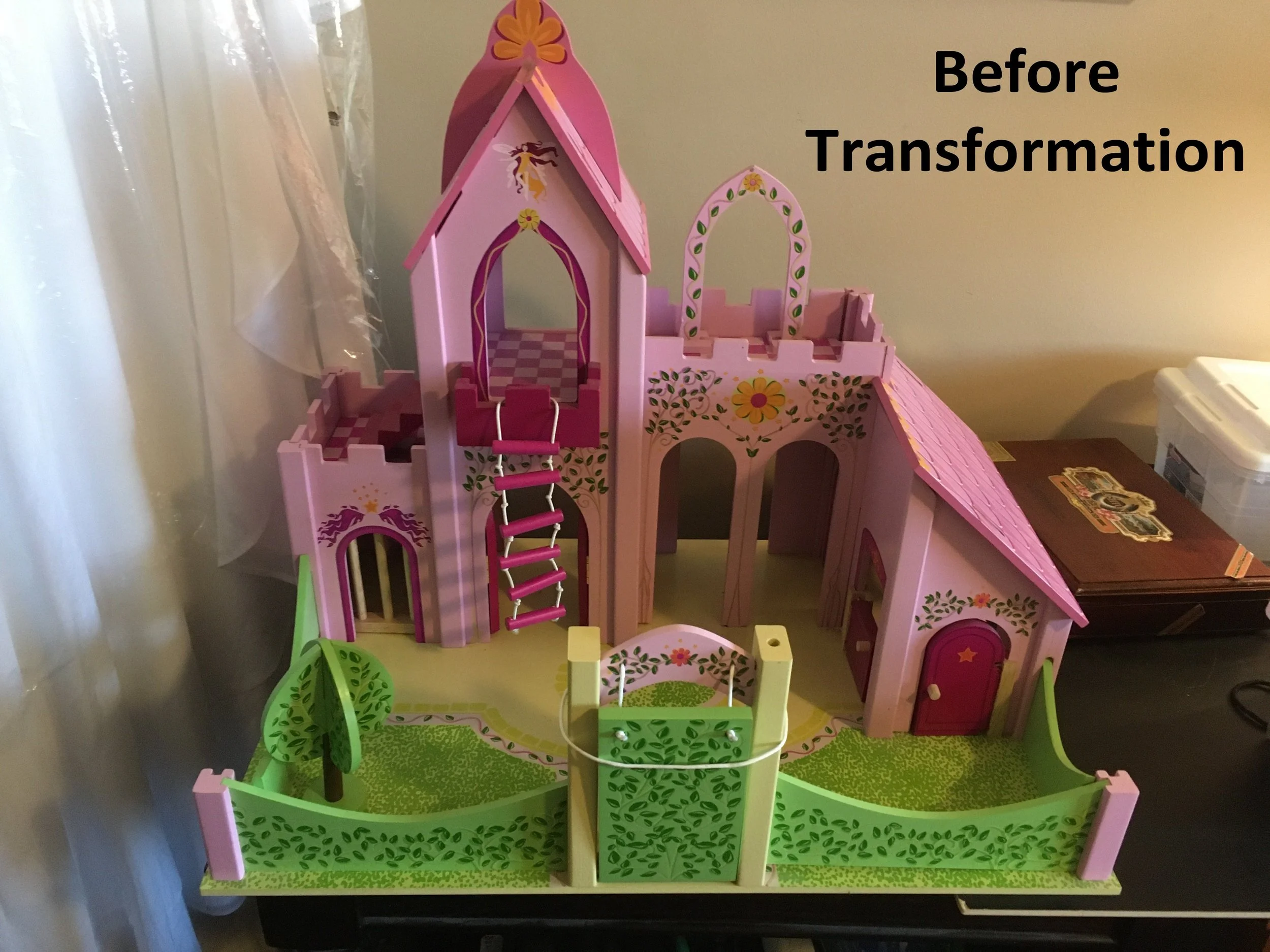 A pink plastic toy castle with a tower, arched doorways, a bridge with a hanging ladder, and a surrounding green fence, placed on a table next to a plastic storage container.