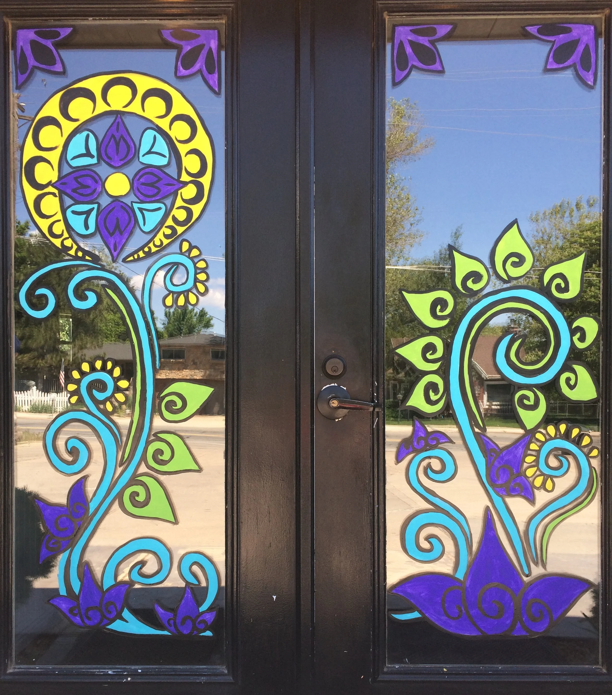 Decorative stained glass window panels with colorful abstract floral and swirl patterns in purple, yellow, blue, and green, set in a black wooden frame.
