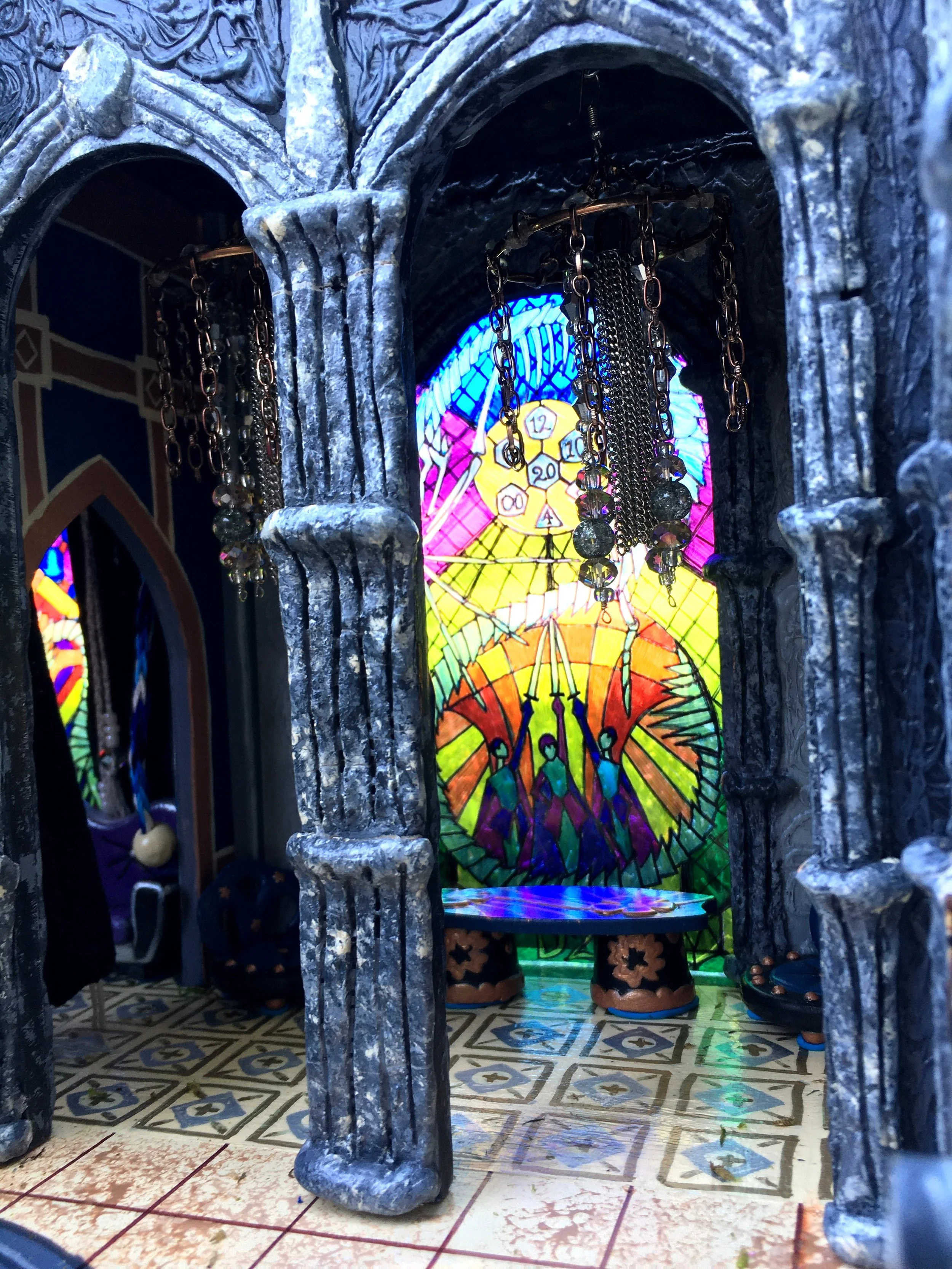 A view through a small iron gate shows a colorful stained glass window with a clock and umbrella design, part of a decorative interior space with patterned floor tiles and pottery.