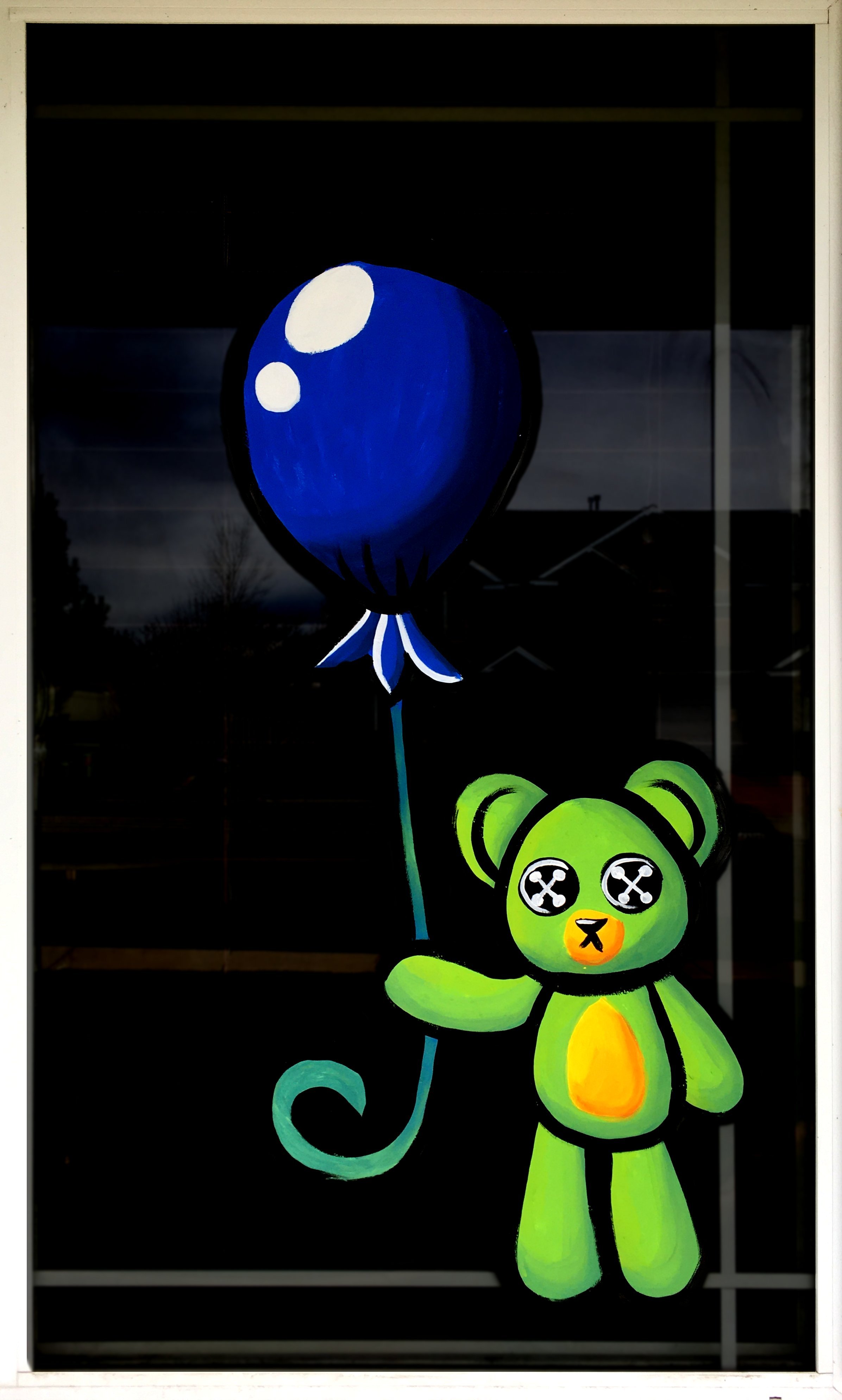 Colorful mural on a window showing a green teddy bear with X's for eyes, holding a blue balloon with white highlights.