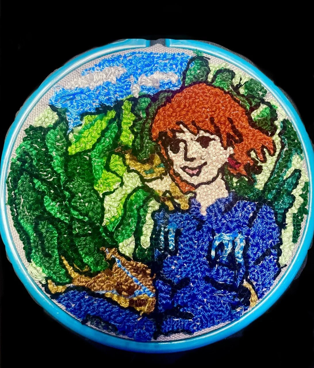 Colorful embroidered design of a person with red hair and a blue shirt, surrounded by green foliage and a blue sky, in a circular frame.