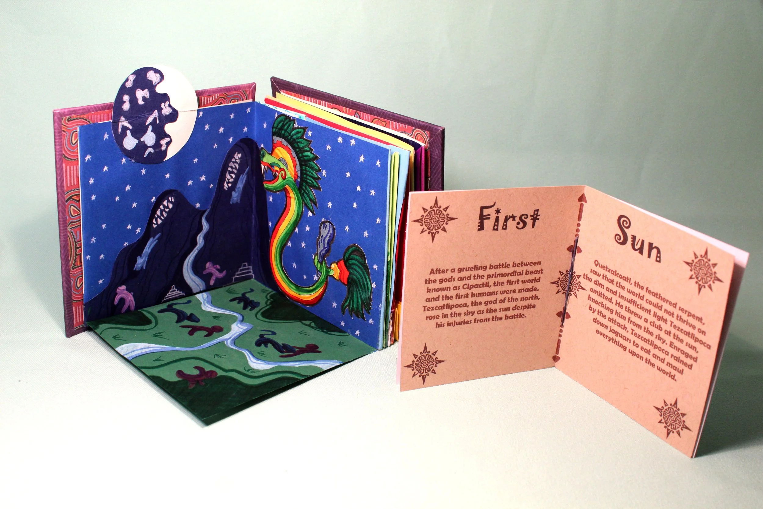 Open pop-up book depicting mythology scene with dragon and mountain, and a pink informational page titled 'First Sun' with text about ancient gods and mythological stories.