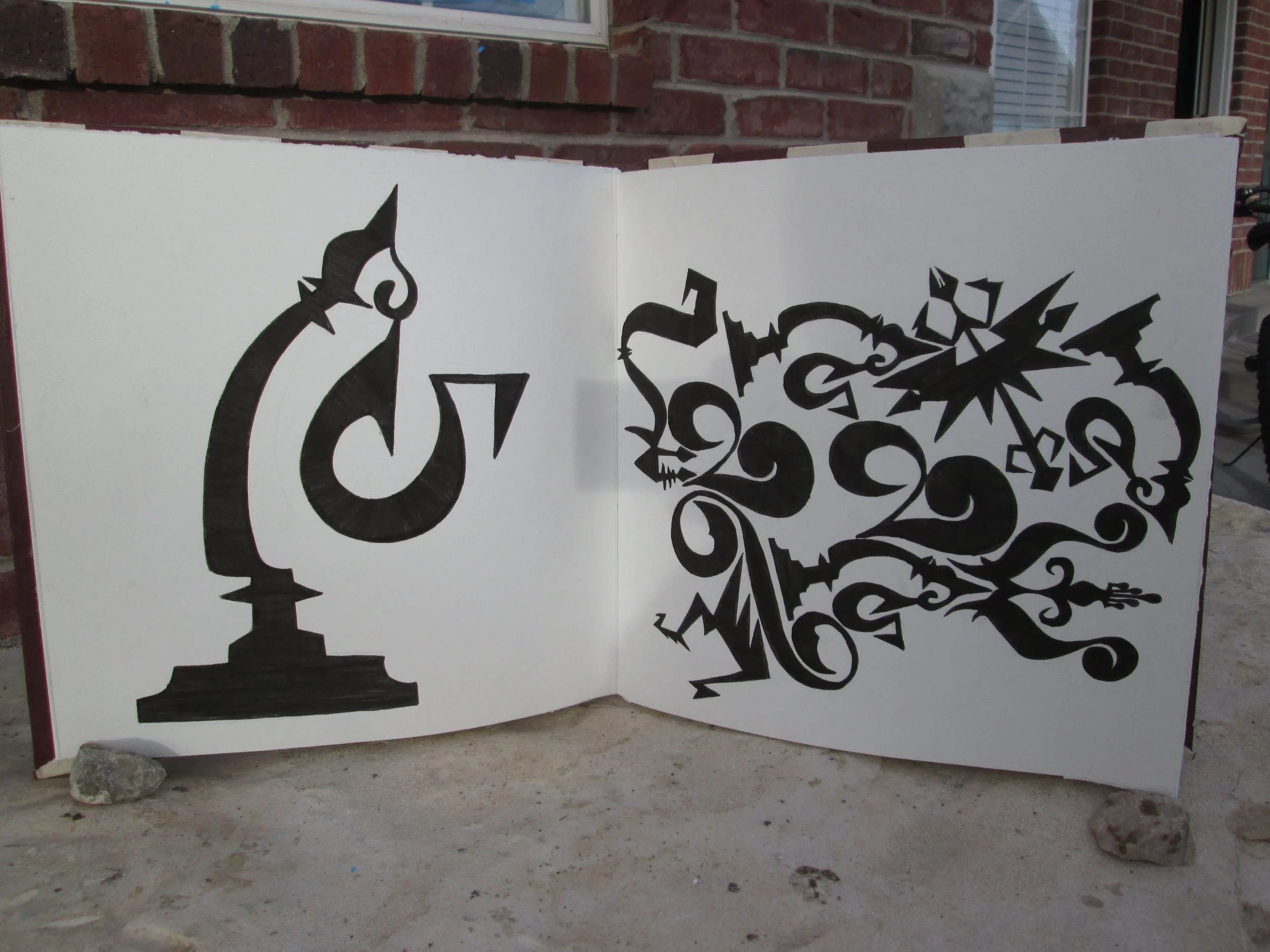 A white panel with black graffiti-style artwork featuring abstract shapes and stars, set outdoors against a brick house wall.