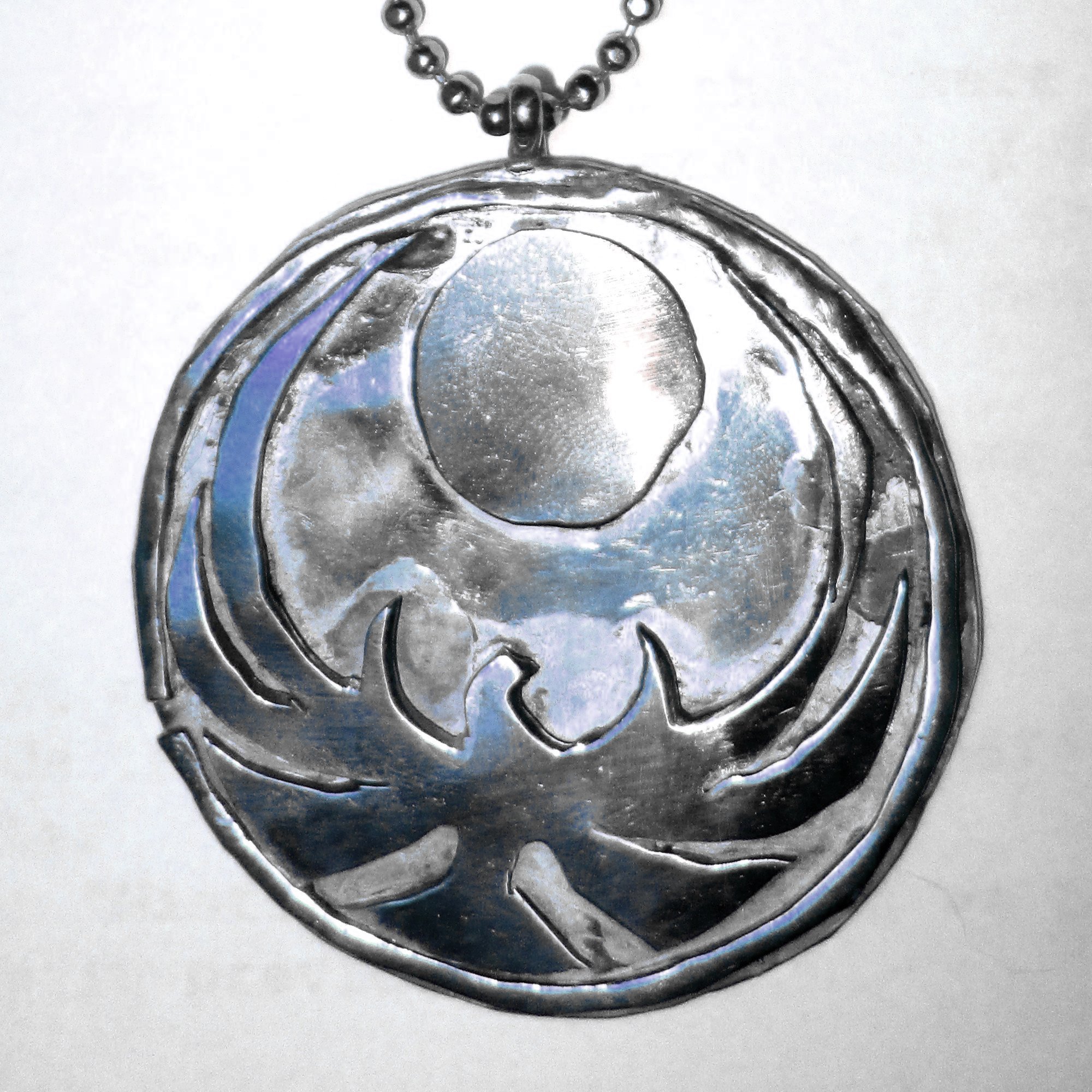Close-up of a metallic pendant with a head in profile and decorative swirl design, hanging from a chain.