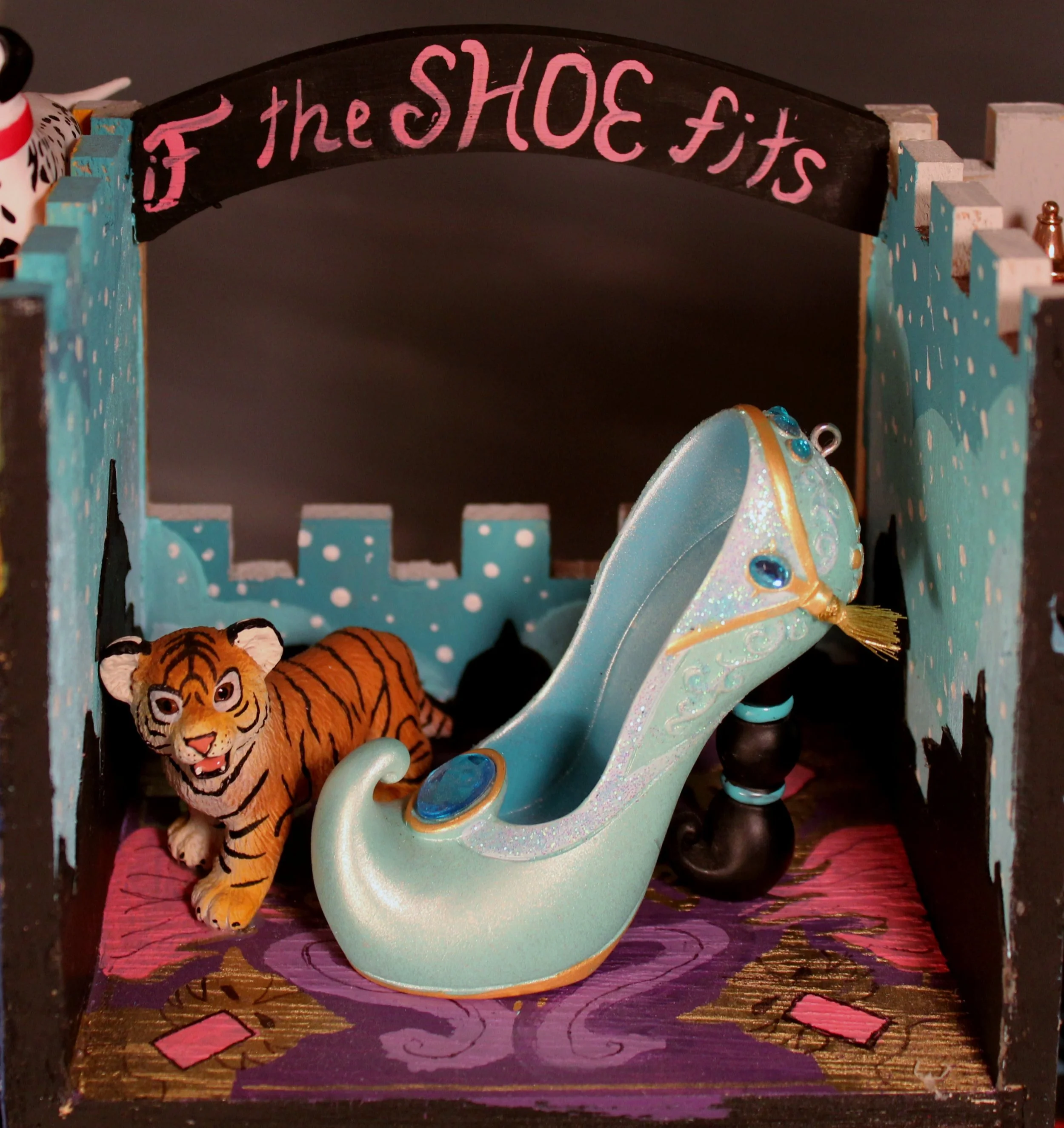 Decorative display with a sign reading 'if the SHOE fits' above a painted background with a toy tiger and a pastel-colored shoe with embellishments.
