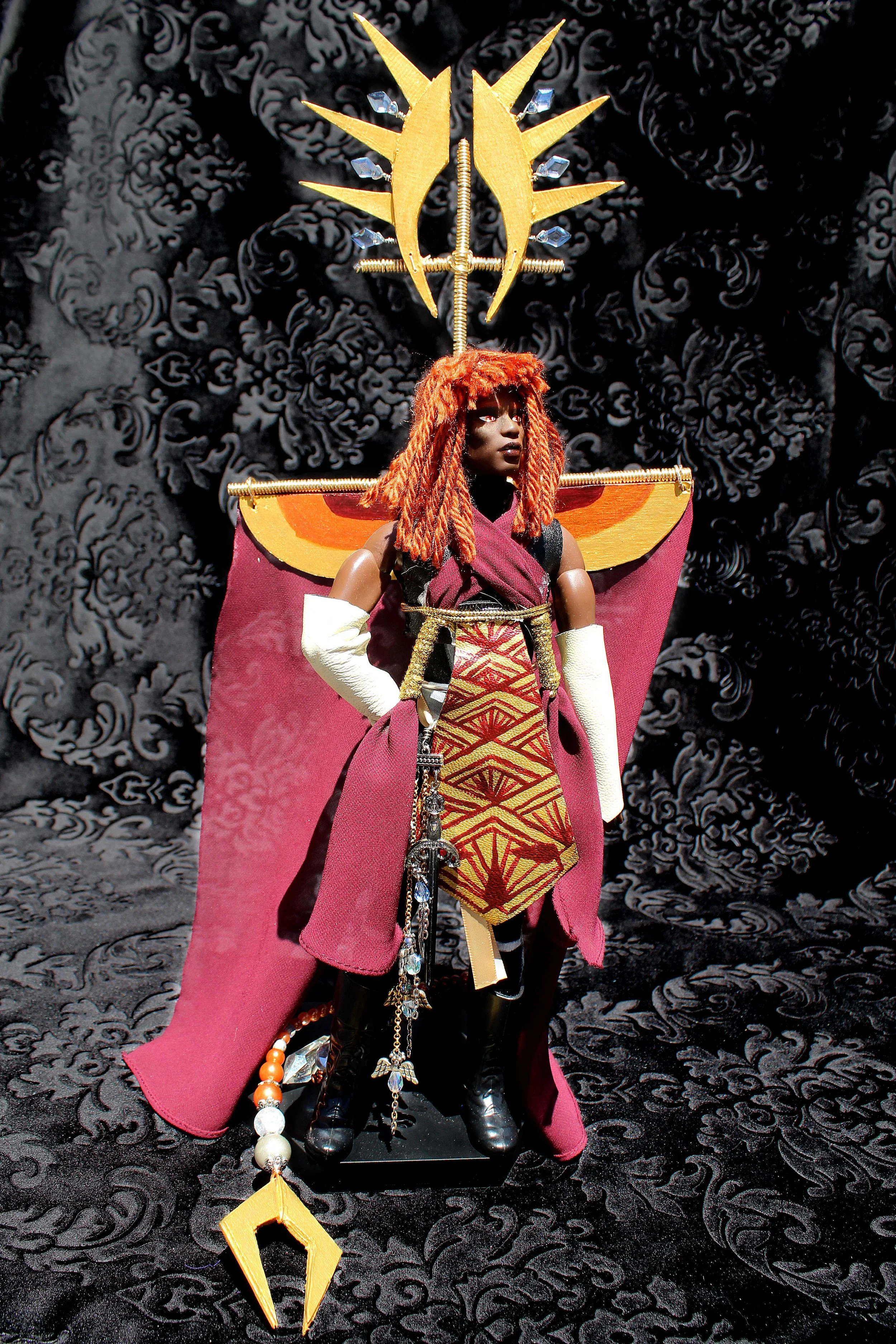 A detailed figure of a fantasy character with red dreadlocked hair, wearing a colorful ornate costume with a cape, standing on a black textured surface with a black ornate background. The character has elaborate accessories and headpiece with gold an