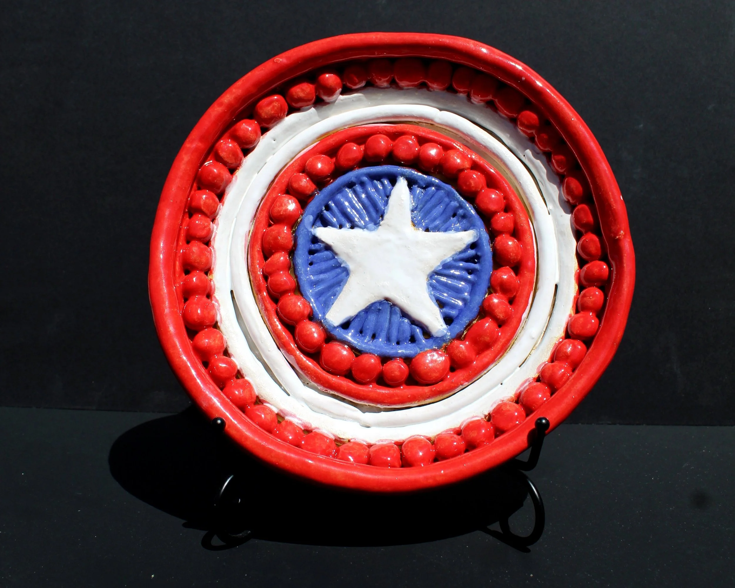Decorative patriotic clock resembling Uncle Sam with red, white, and blue colors, featuring a white star at the center, surrounded by red beads and a red border, against a black background.