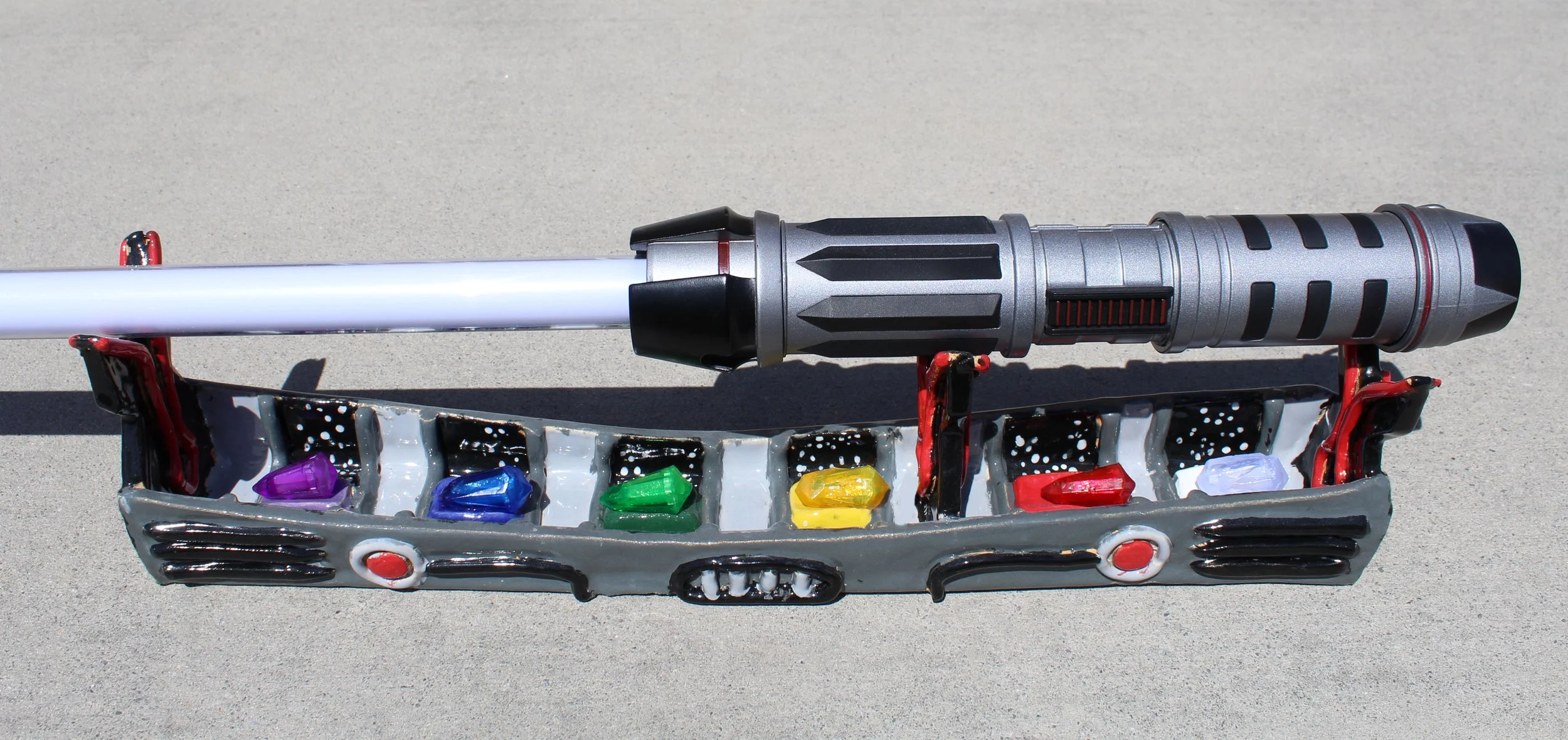 A toy lightsaber resting on a toy car with small colored gems inside it, placed on a gray surface.