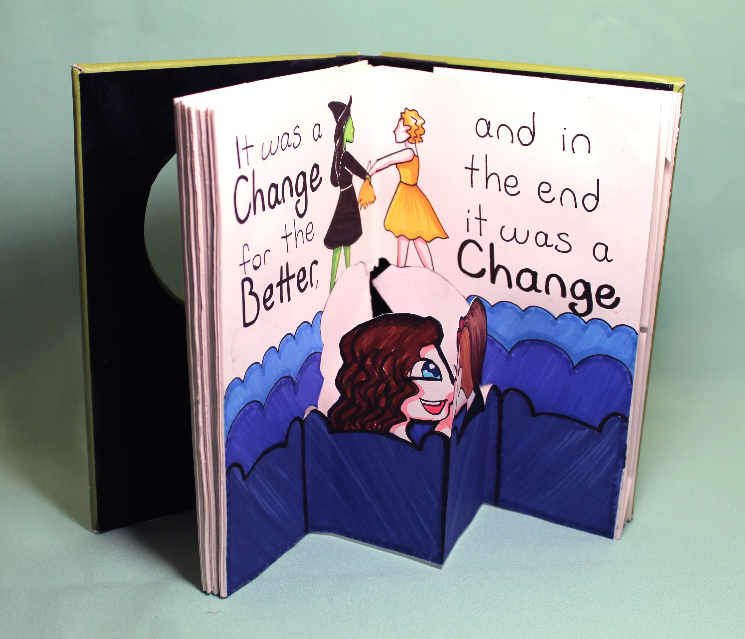 Open illustrated storybook with handwritten text and colorful drawings of two characters, one in a witch hat and another in a dress, standing on clouds.