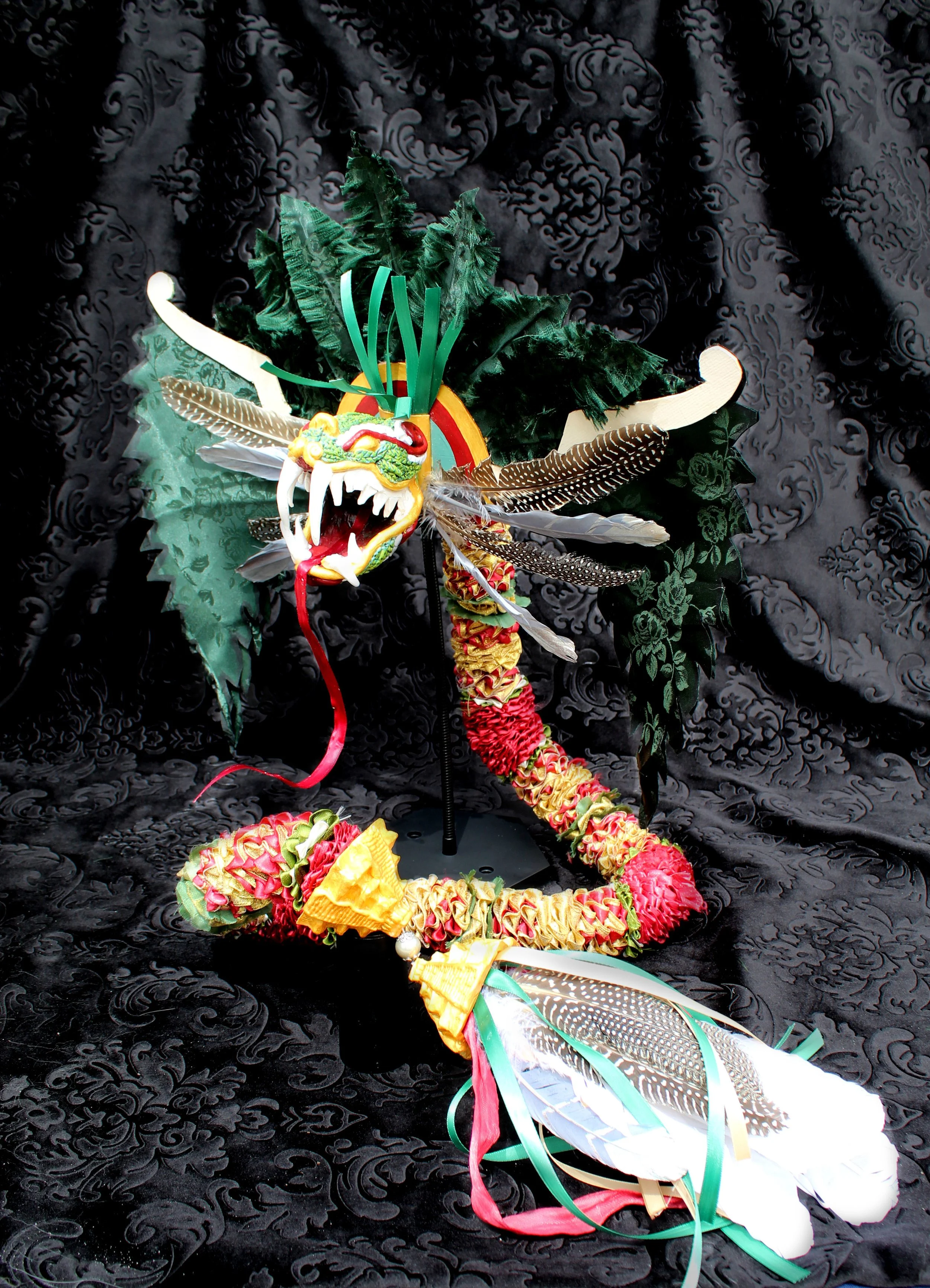 Colorful dragon dance costume with feathers, ribbons, and a dragon face ornament, on a black patterned fabric background.