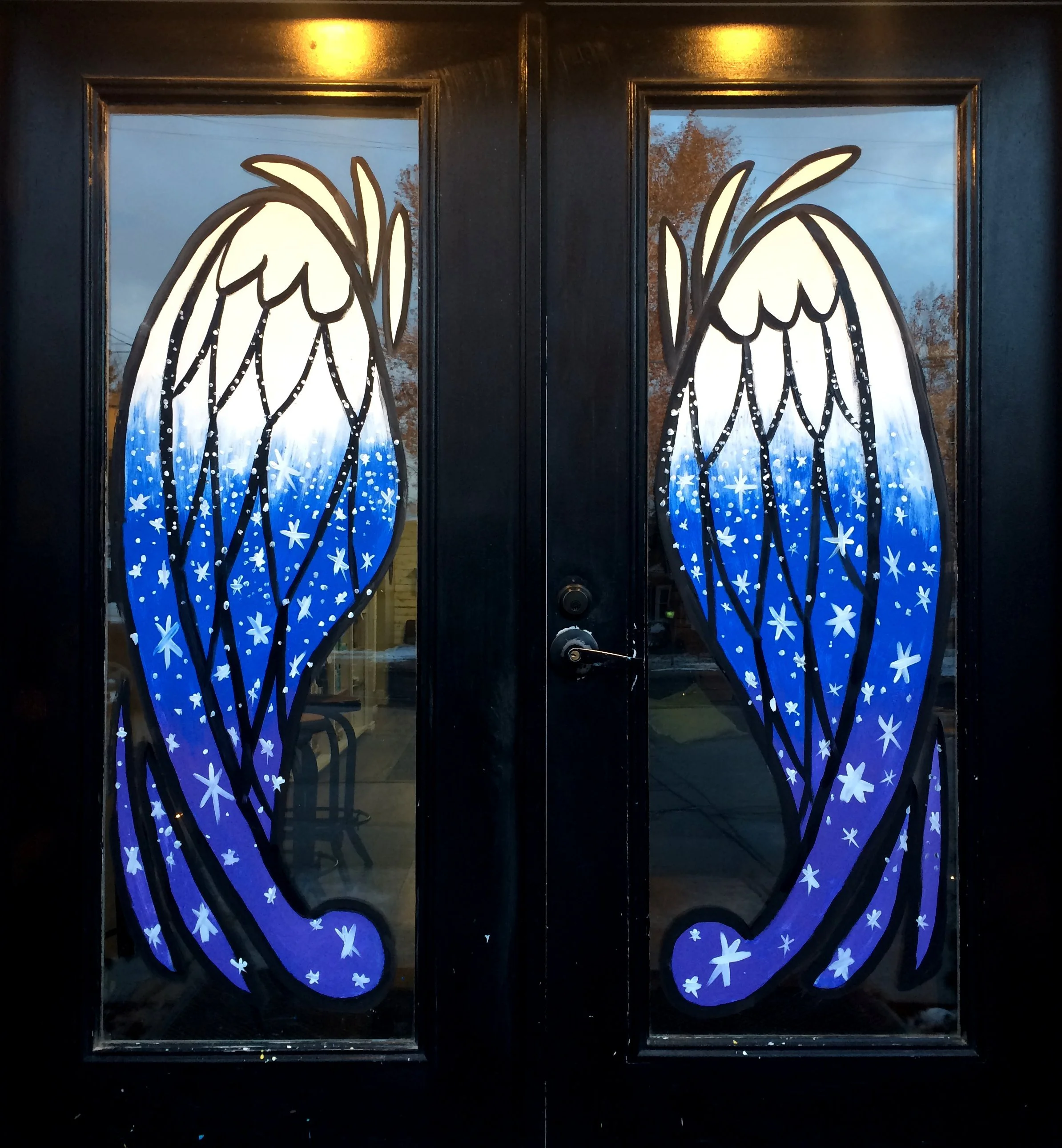 Decorative black door with art featuring white angel wings with black outlines and blue background adorned with white stars.