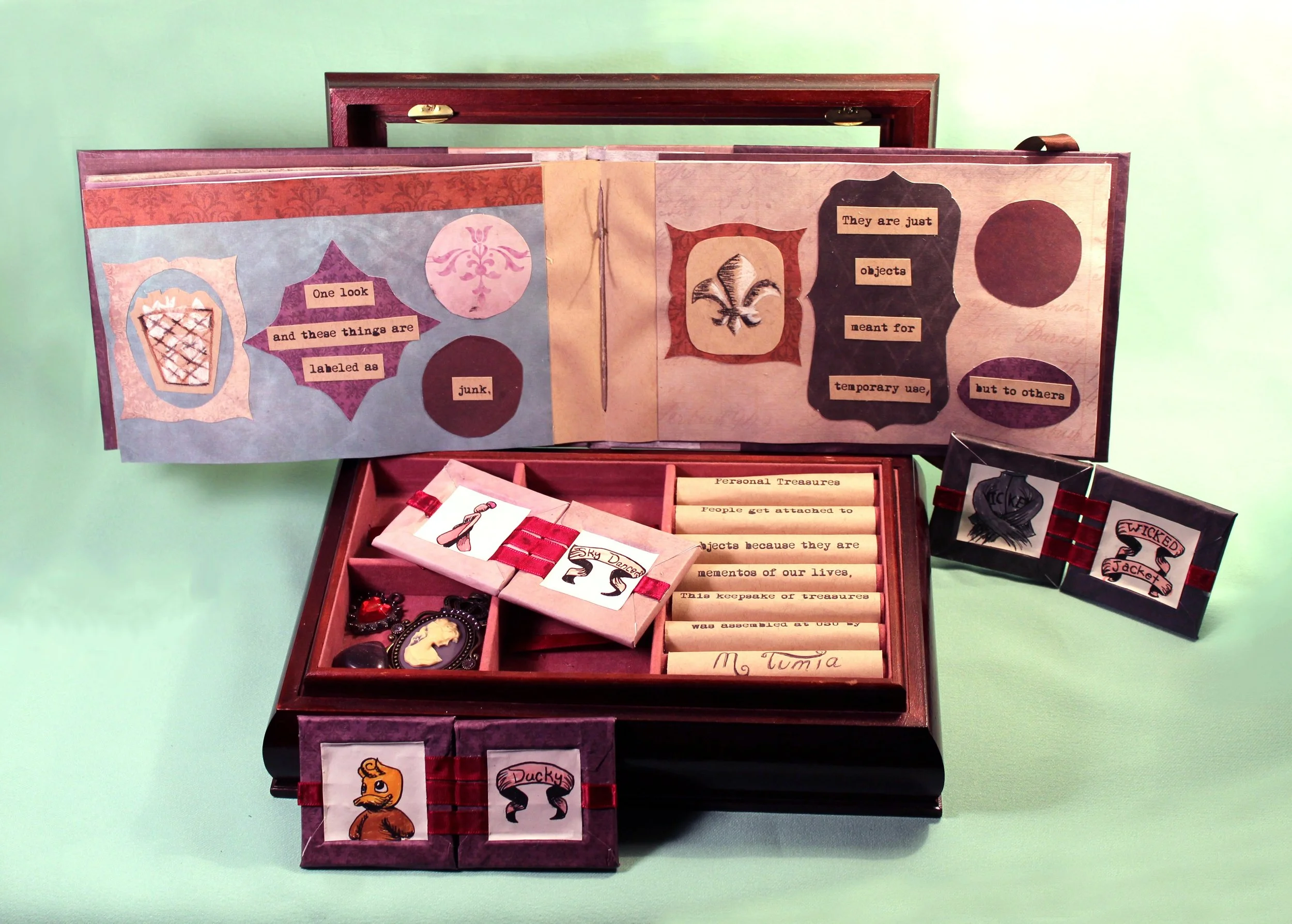 Open wooden box with handmade paper inserts featuring text and illustrations about objects labeled as junk or treasures, including a cameo brooch and themed cards.