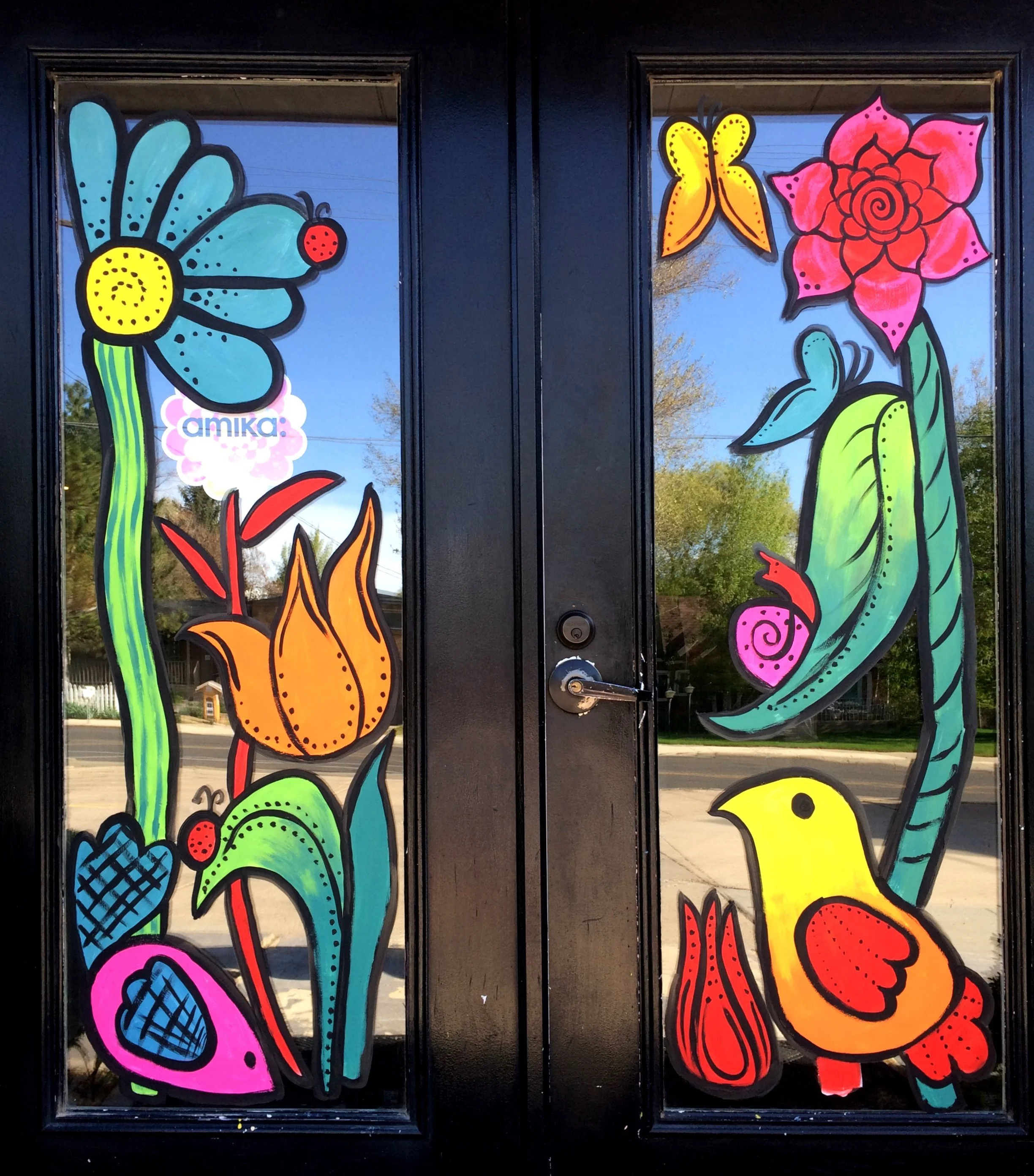 Colorful window art featuring large flowers, butterflies, and a chick, with the name 'amika' at the bottom left.