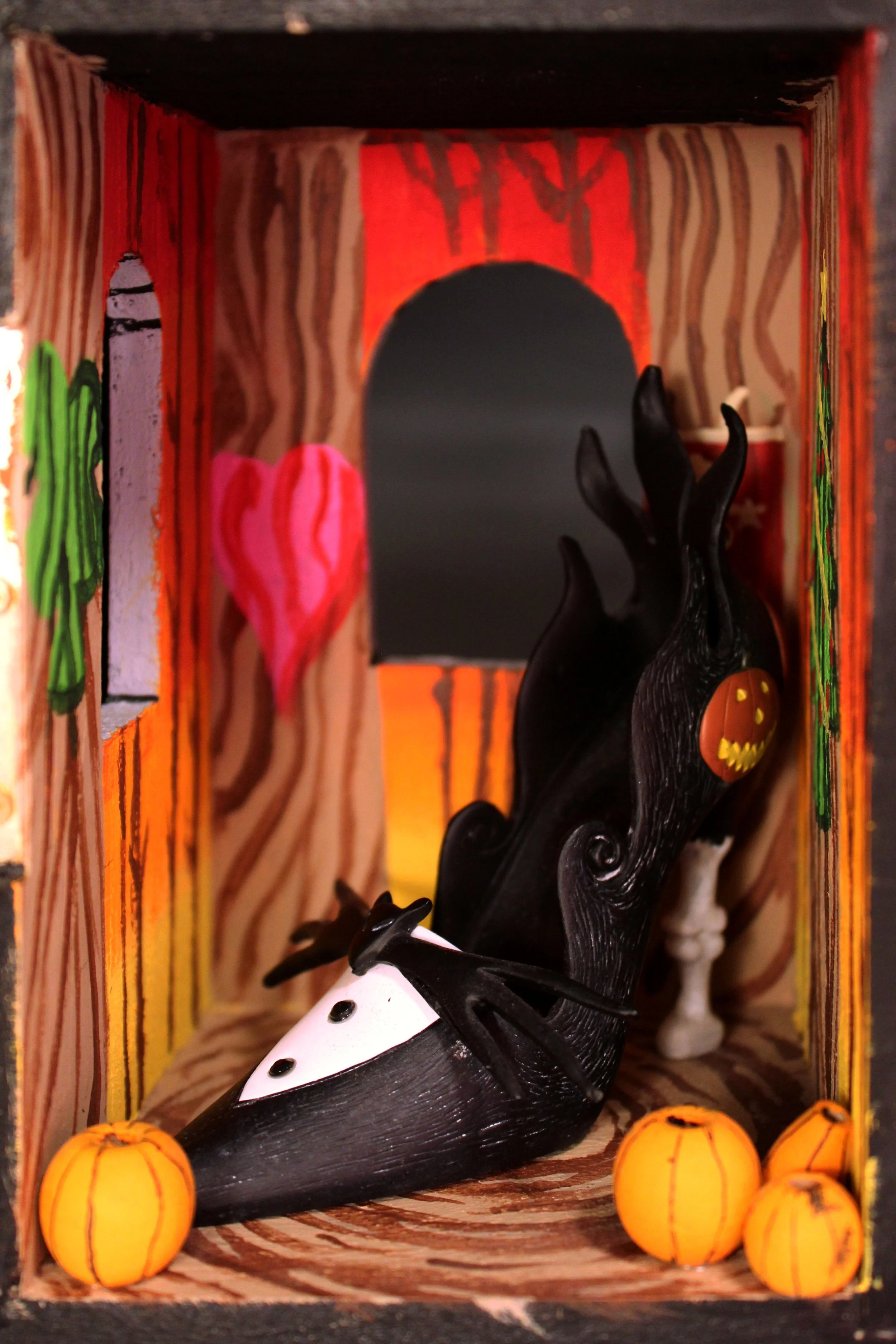 A black witch figurine with a carved pumpkin face on its side, surrounded by small orange pumpkin decorations, inside a decorated box with Halloween-themed artwork.
