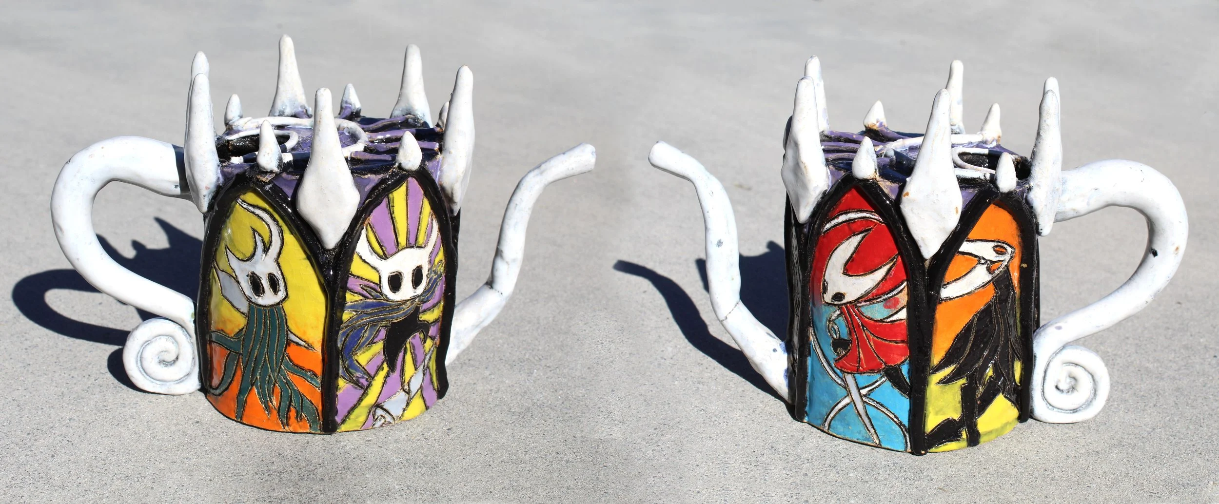 Two decorated ceramic mugs featuring colorful skeleton and themed artwork, placed on a sandy surface.