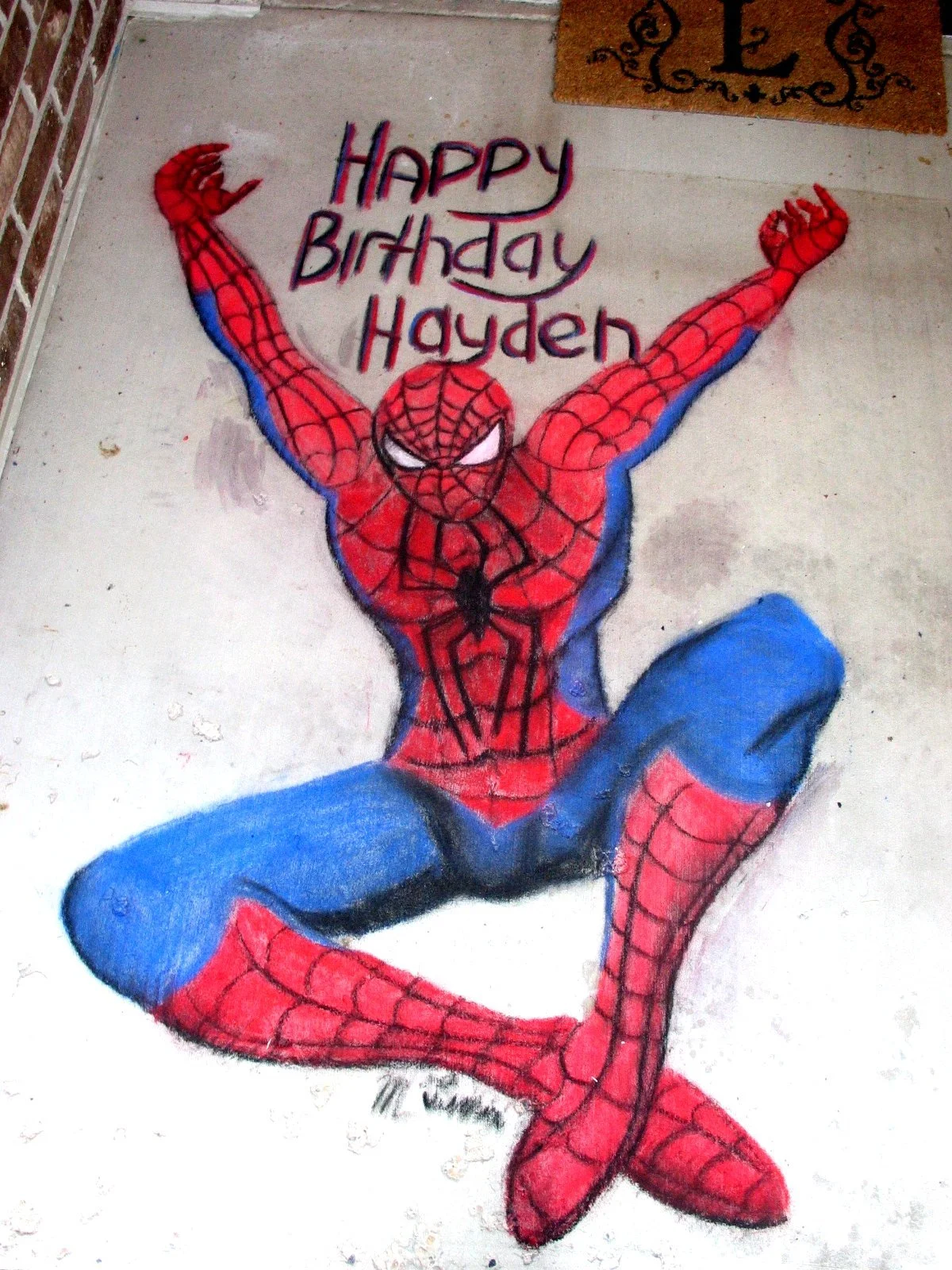 A colorful chalk drawing of Spider-Man in a dynamic pose with arms raised and legs bent. The words 'Happy Birthday Hayden' are written above him.