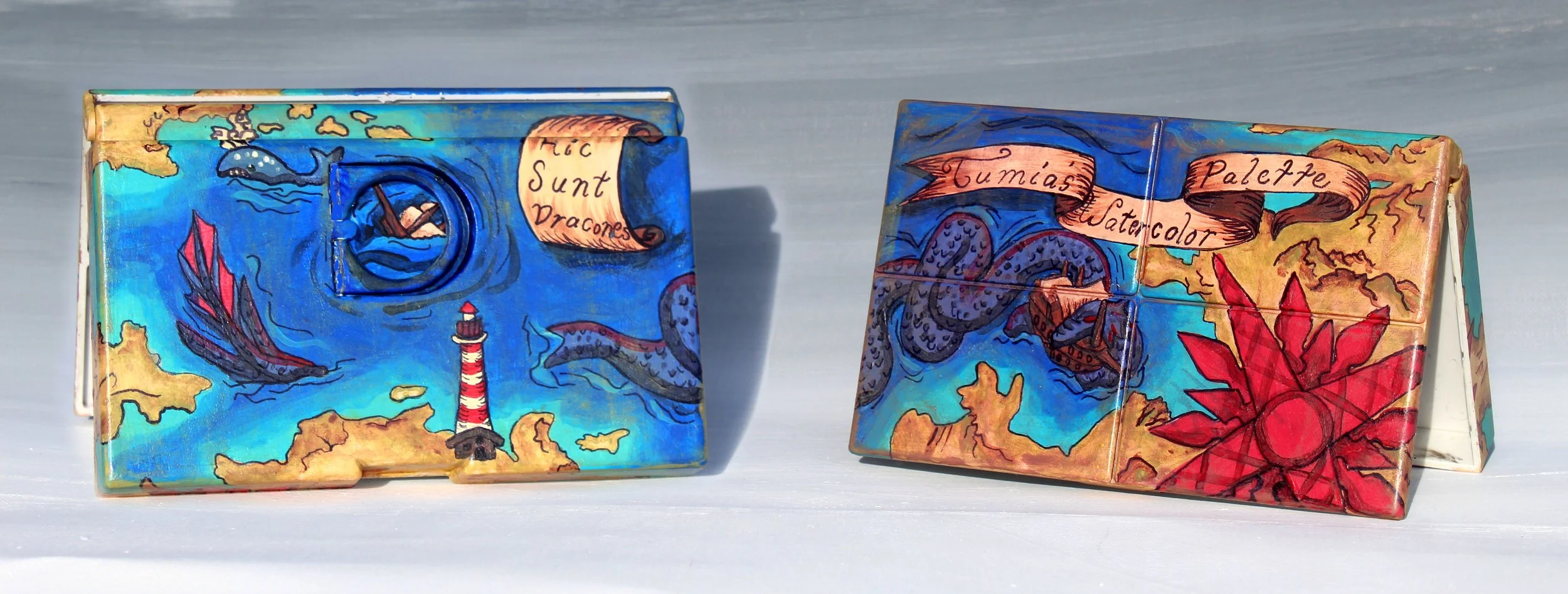 Colorful painted tiles depicting a nautical scene with a lighthouse, sea creatures, and a map with labels in Spanish, including 'Sunt Dragones', 'Gumas', 'Watercolor', and 'Palette'.