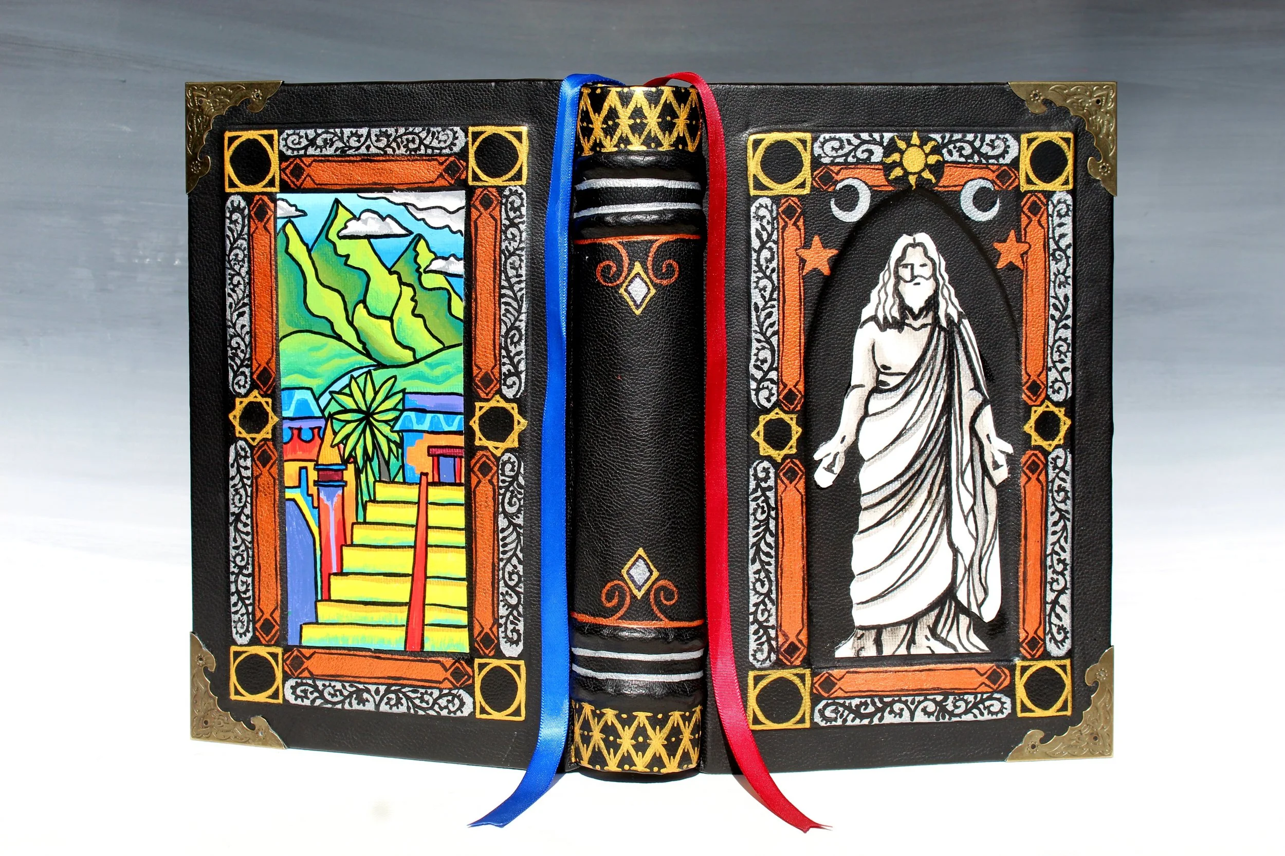 Decorative black folder with detailed gold corners, colorful stained glass artwork of a mountain landscape on the left, a black and white image of a woman on the right, and a central strap with gold patterns and blue and red ribbons.