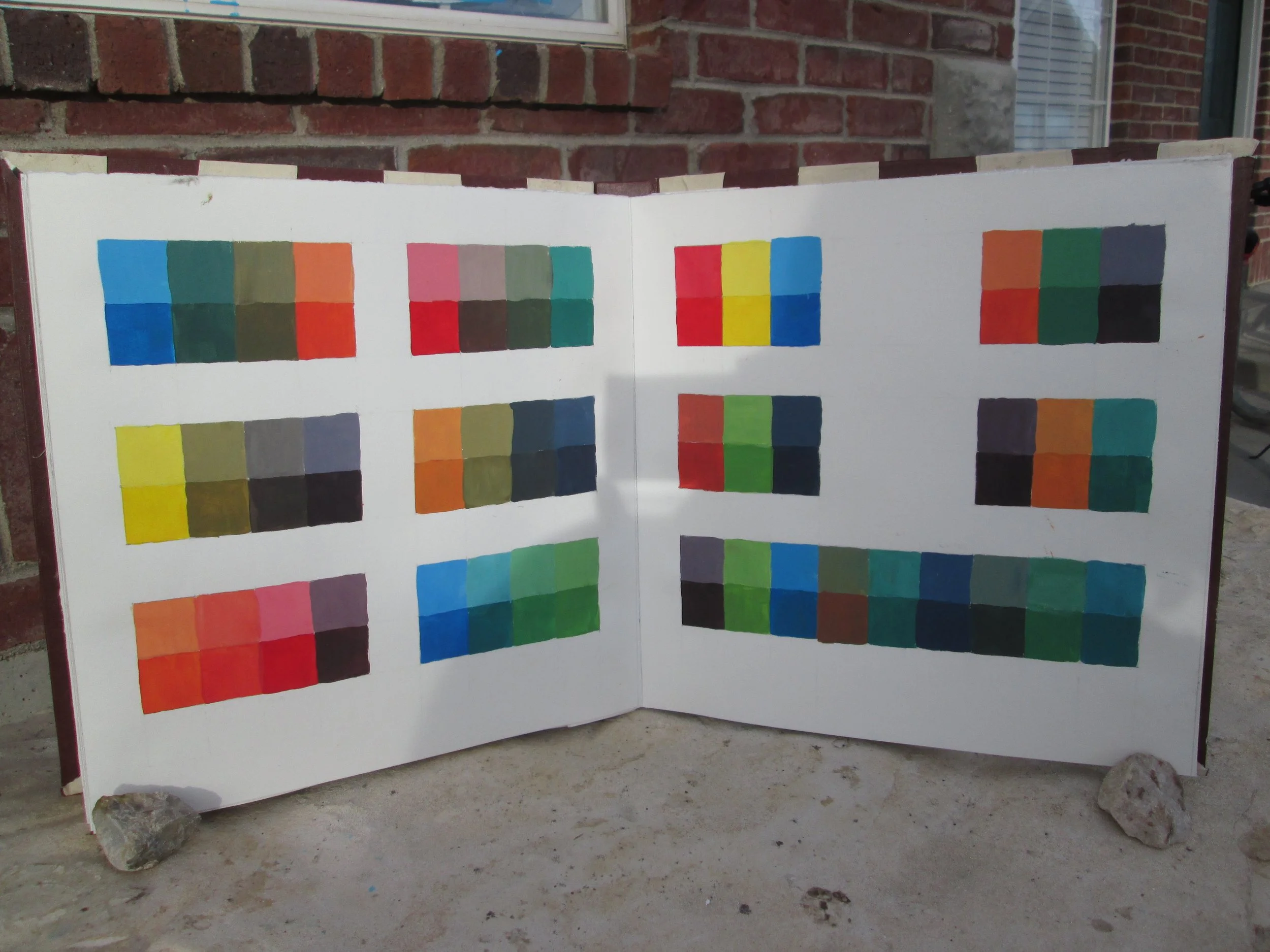 Open book or display with color charts attached outside in front of brick wall, with rocks on the ground.