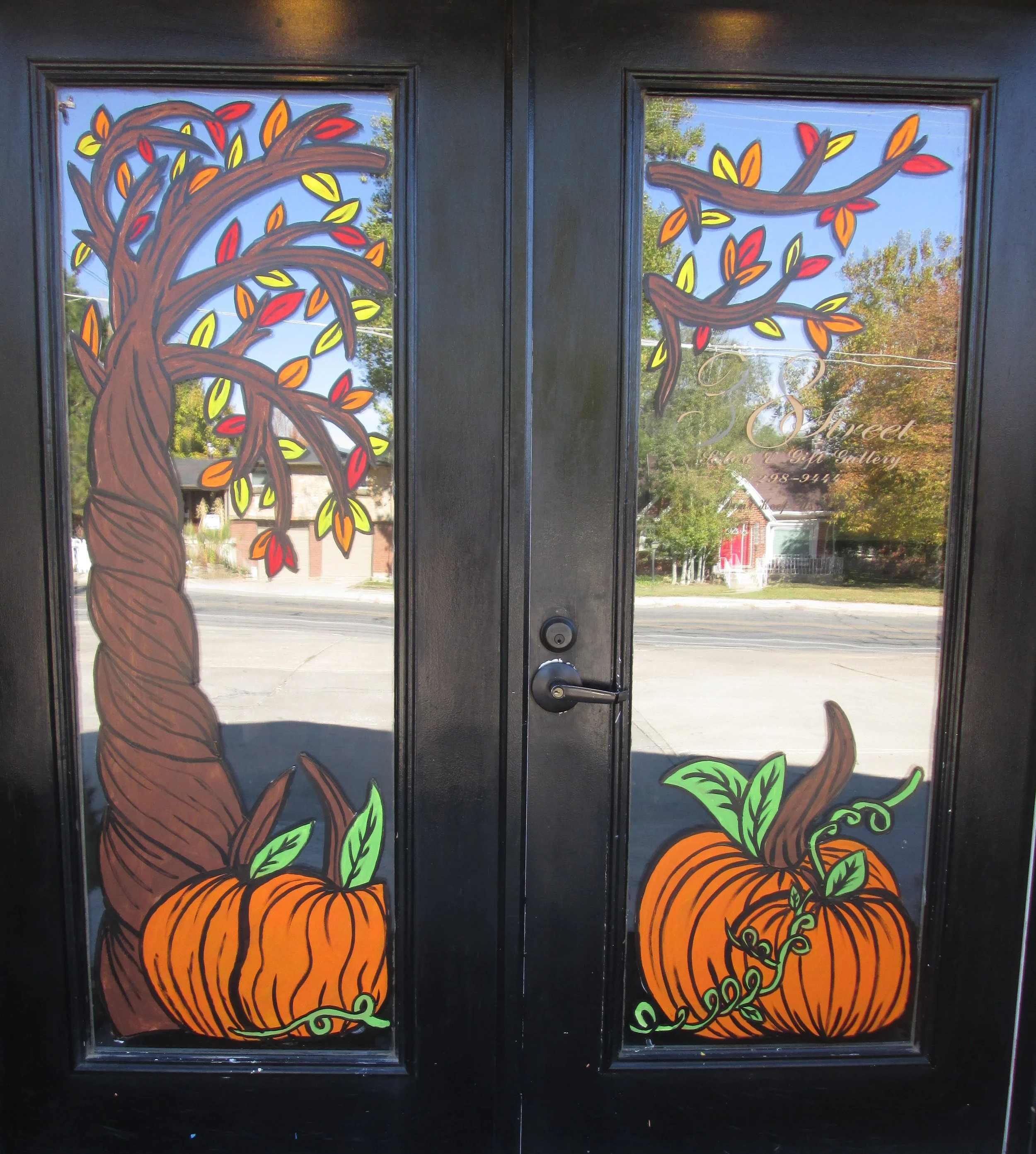 Decorative black door with colorful painted pumpkins, green vines, and autumn leaves, featuring a tree with orange, red, and yellow leaves, and text that reads 'Sweet.'