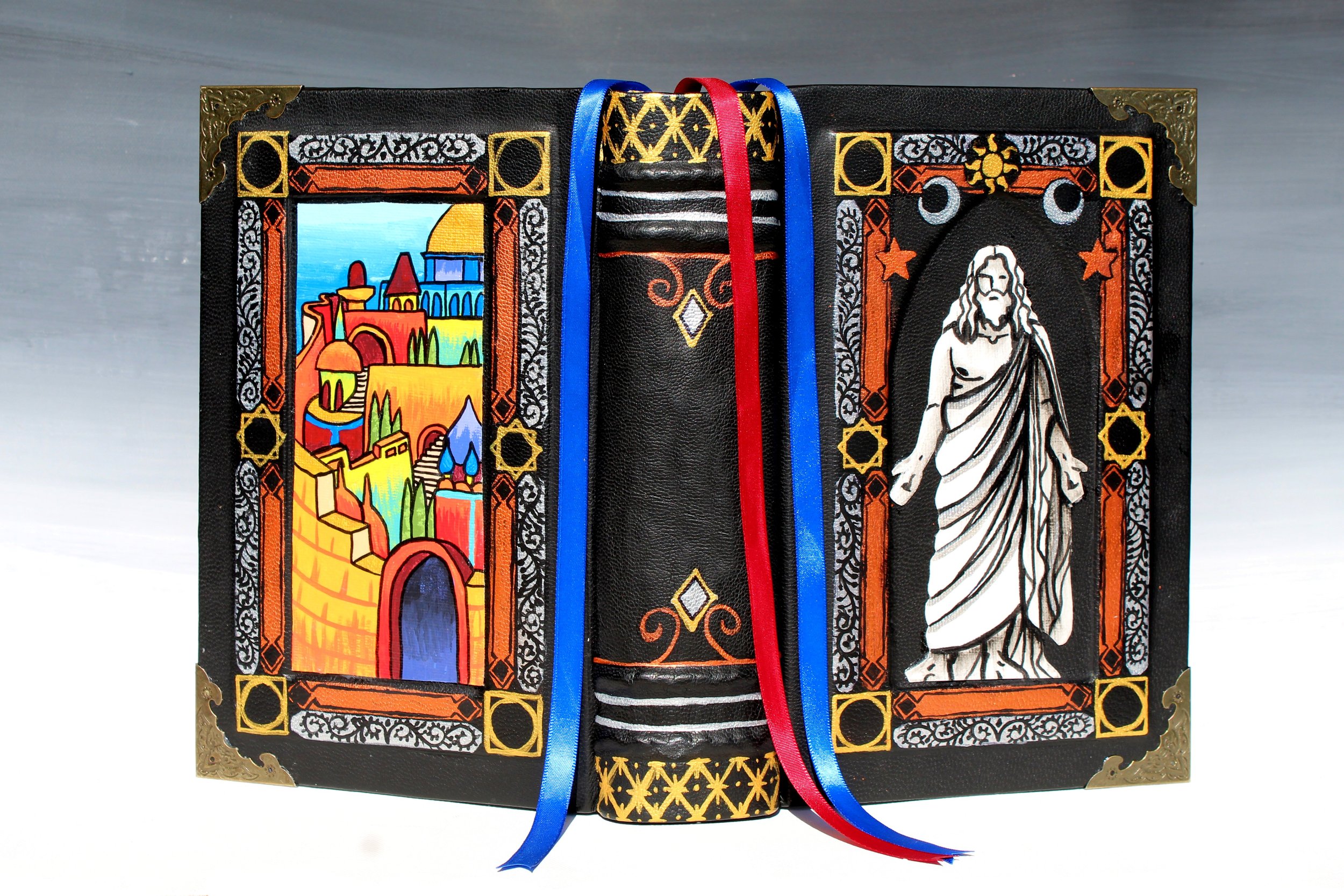 Decorated black box with colorful illustrations of a cityscape on the left, a religious figure on the right, gold metal corners, and blue and red ribbons.