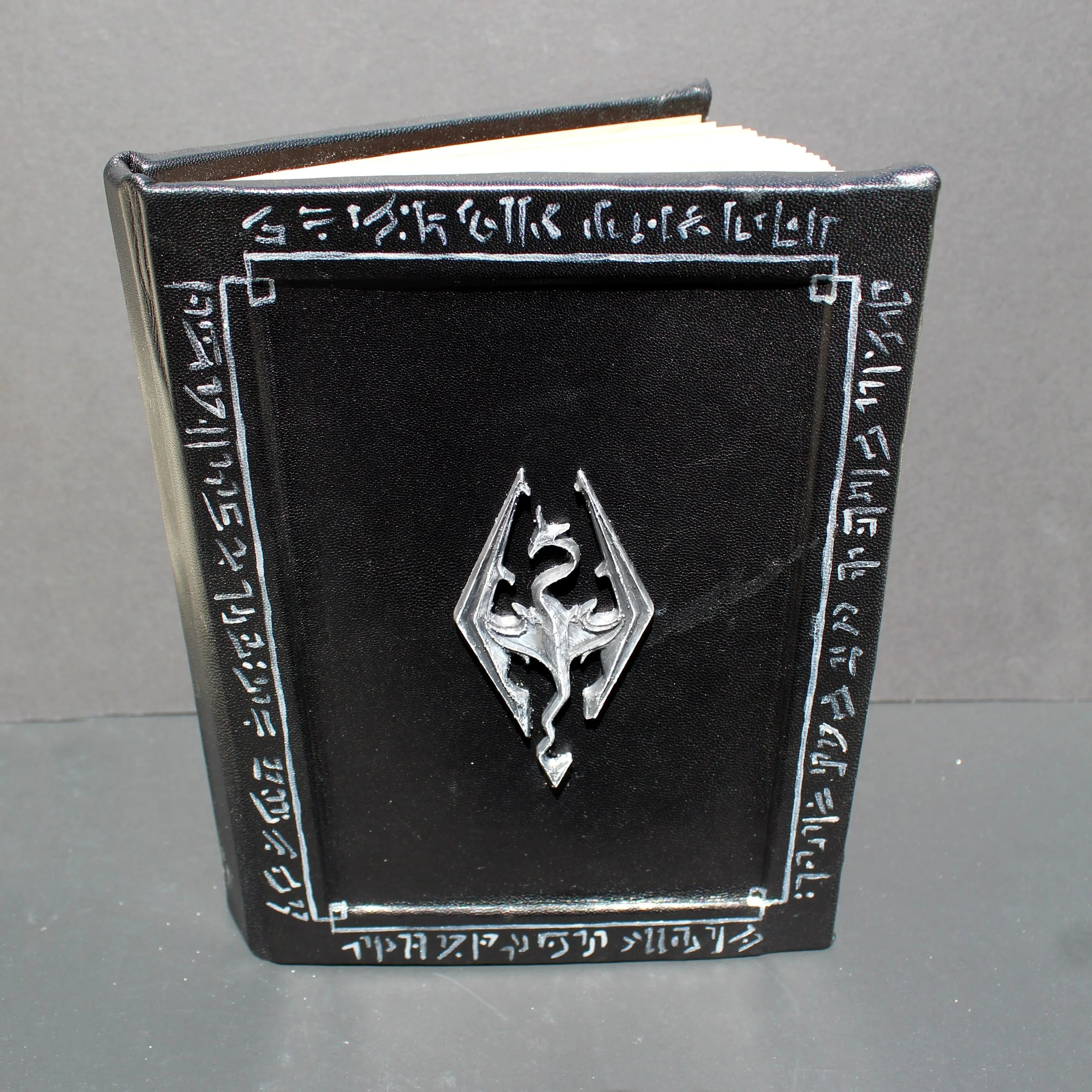 A black tarot card box with white symbols and text, and a metallic sword charm on top, on a gray surface.