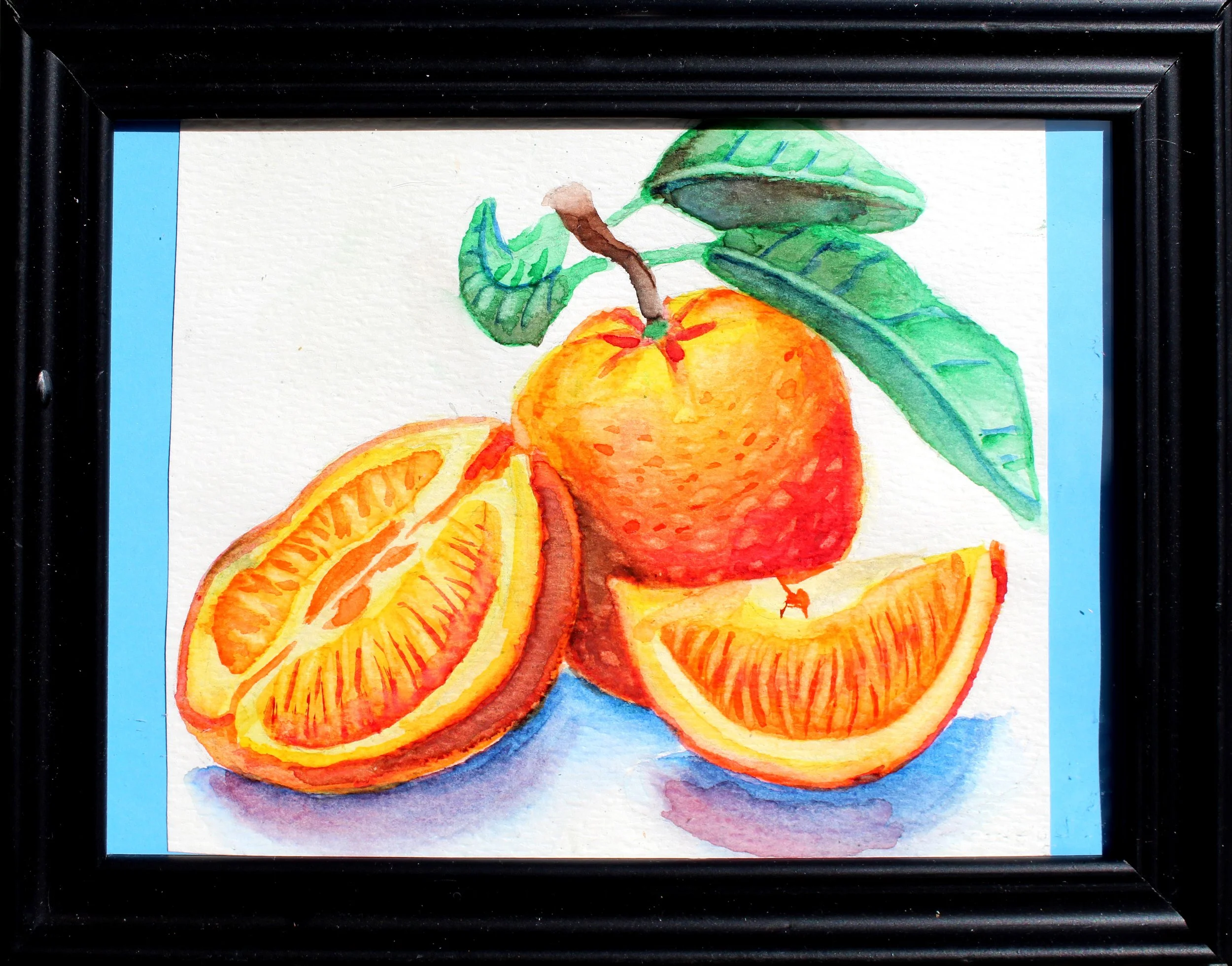 Watercolor painting of sliced oranges on a blue surface with green leaves at the top, framed in black.