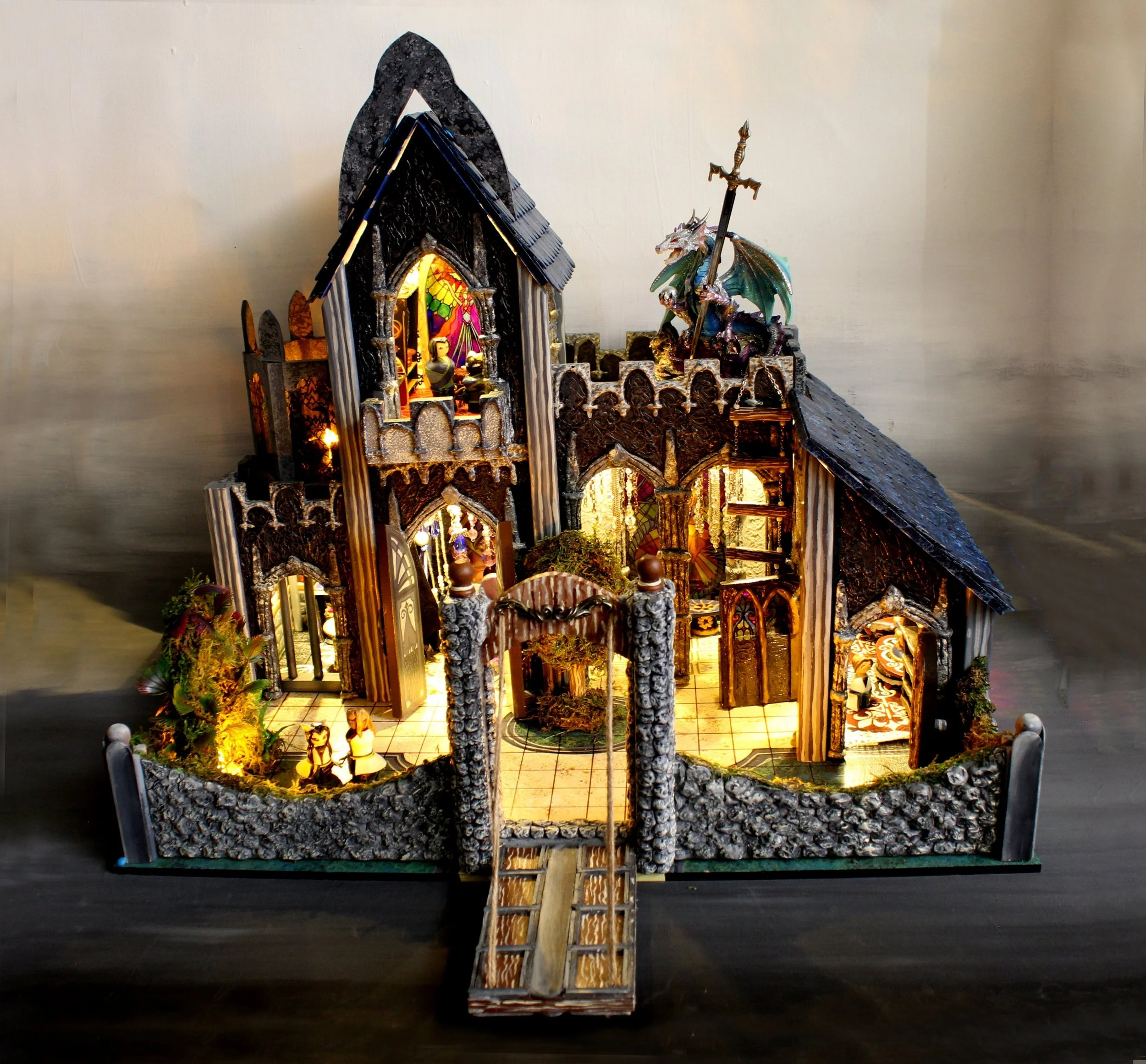 A detailed model of a castle with gothic architecture, including towers, a dragon sculpture holding a sword, and illuminated windows and rooms.