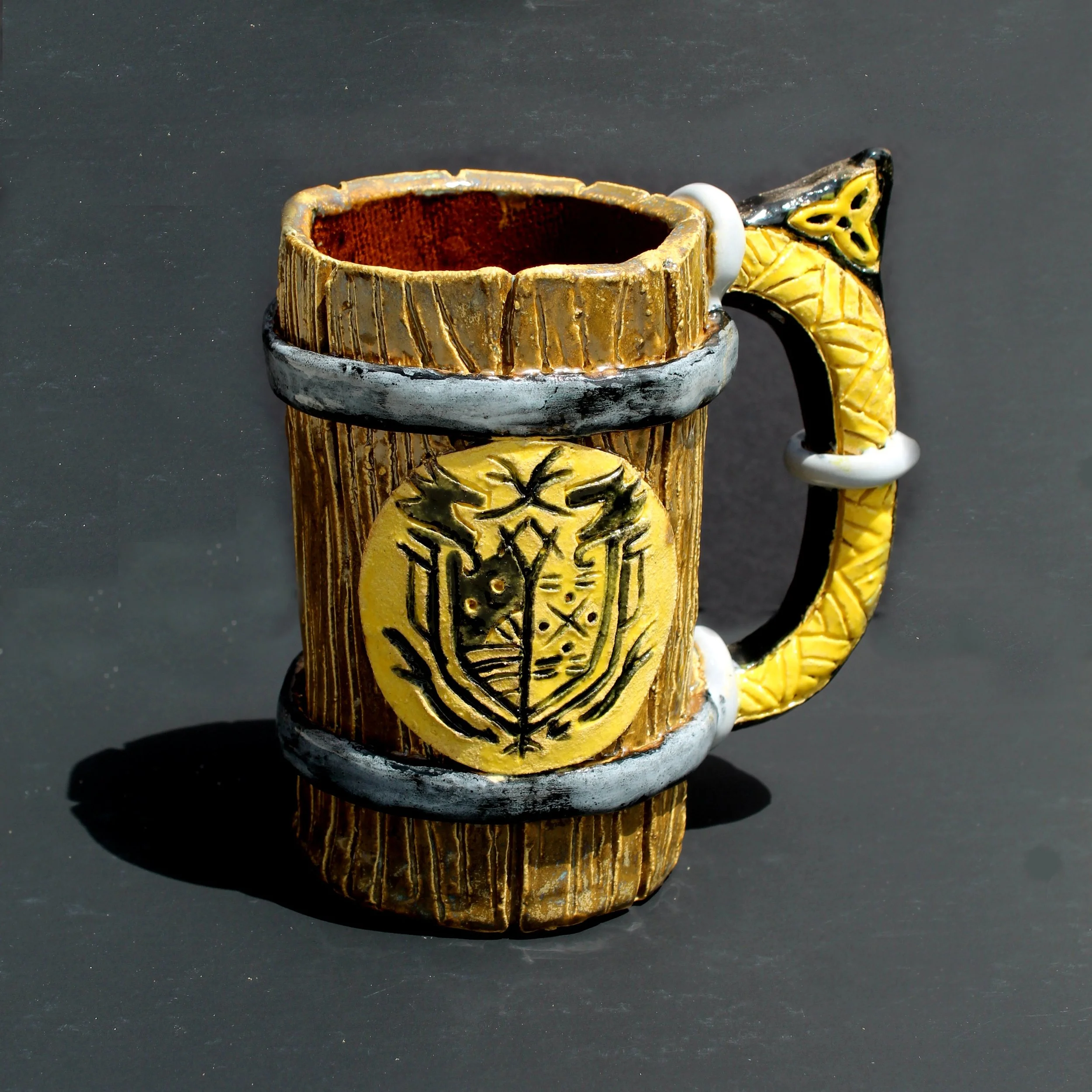 Decorative ceramic mug with a tree pattern painted on yellow and black, placed on a dark surface.