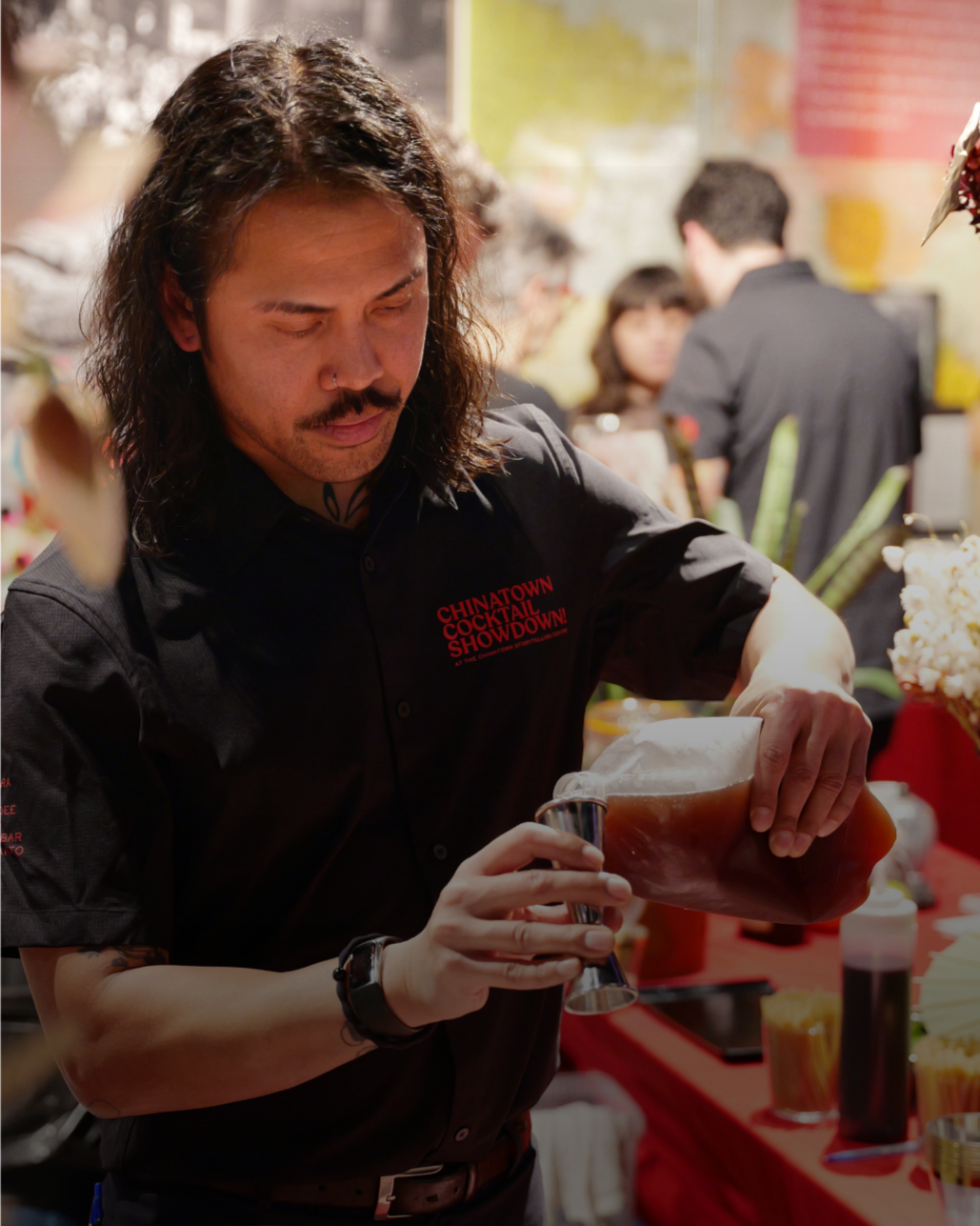 A bartender pouring beer from a tap at a Chinatown Cocktail Showdown event, with people in the background.