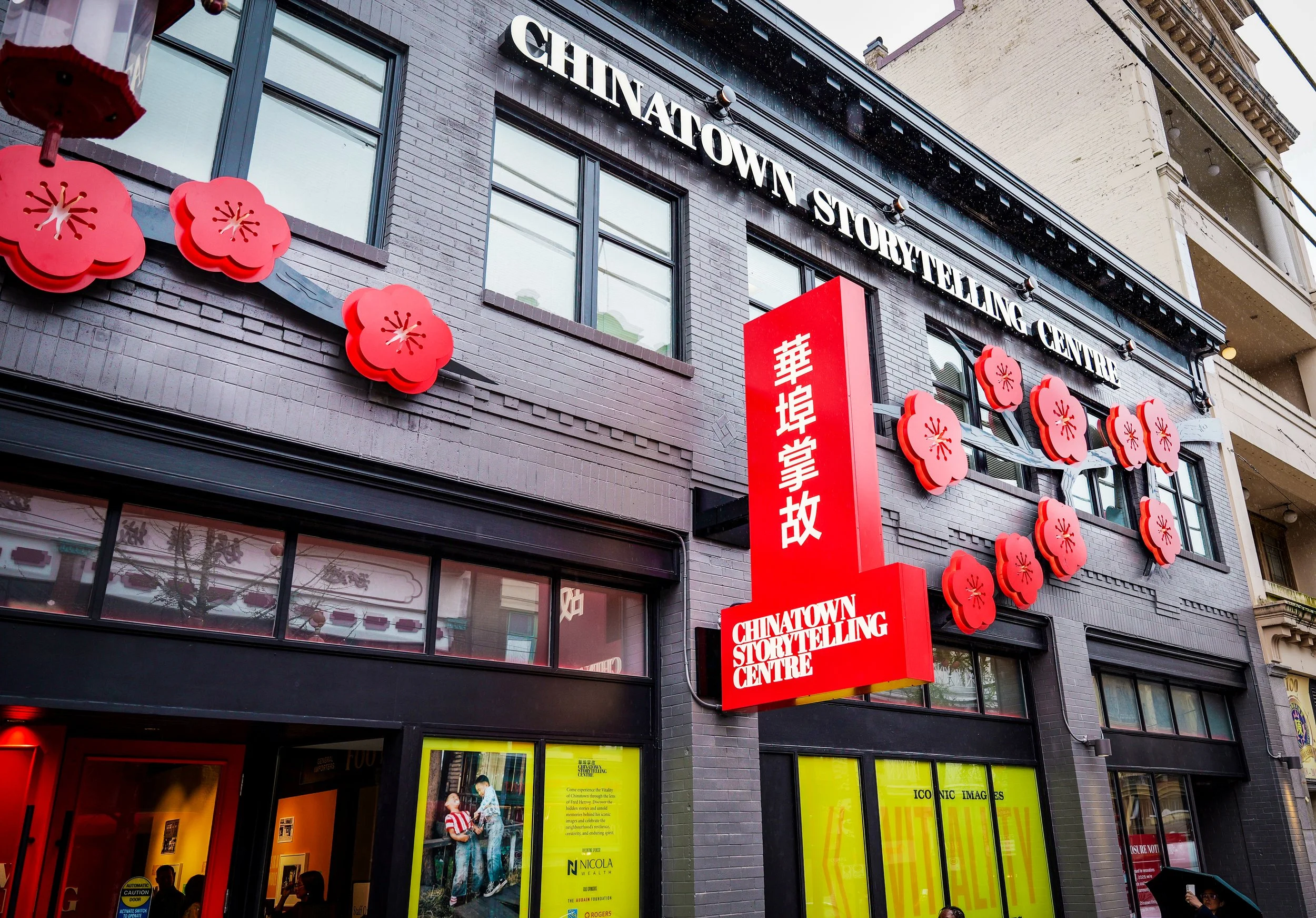 Street view of a building with a sign for Chinatown Storytelling Centre, decorated with red cherry blossom ornaments.
