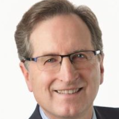 A smiling man with glasses, light brown hair, and a suit against a white background.