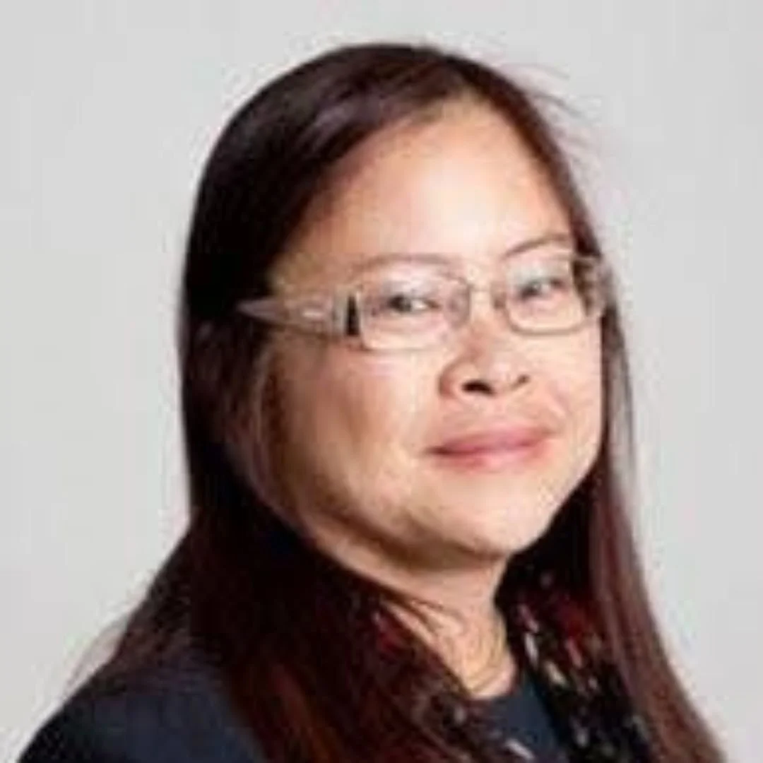 Portrait of an Asian woman with long dark hair, wearing glasses and a black top, smiling subtly.