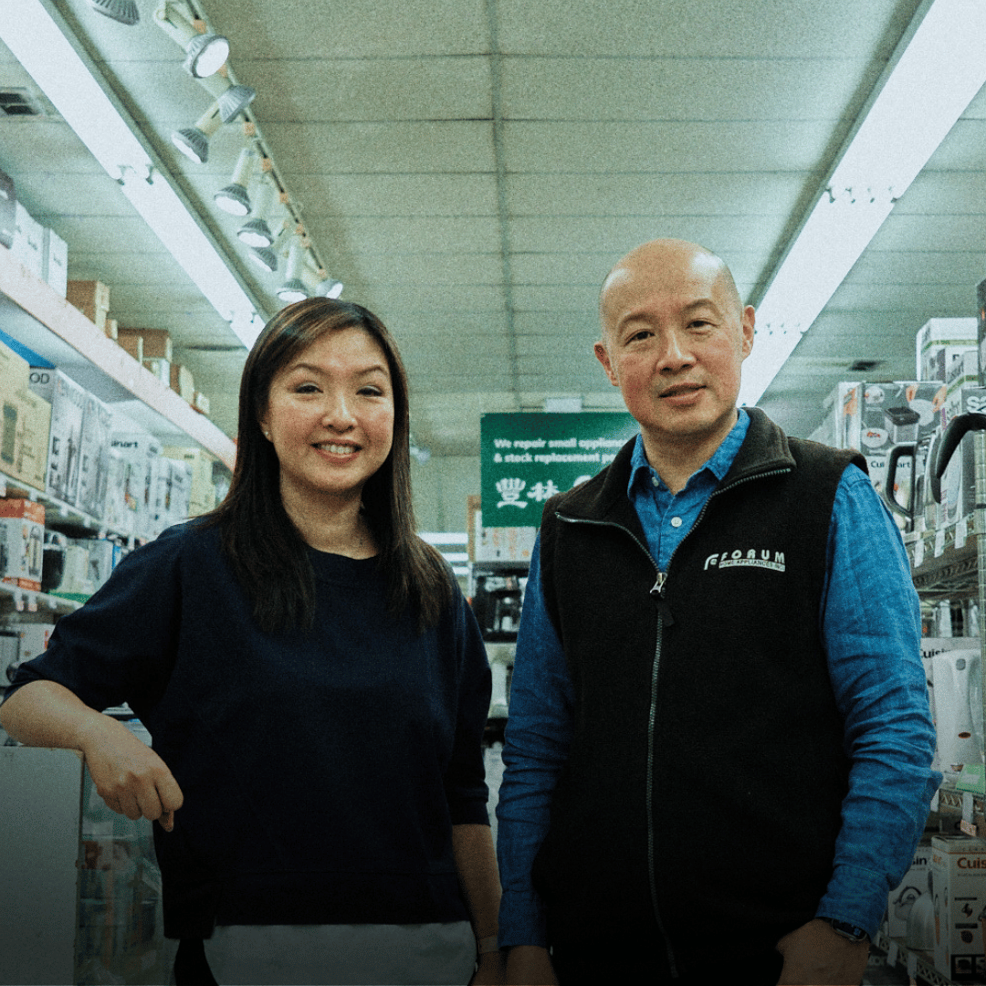 A woman and a man standing together inside a store, surrounded by shelves with various store products, smiling at the camera.