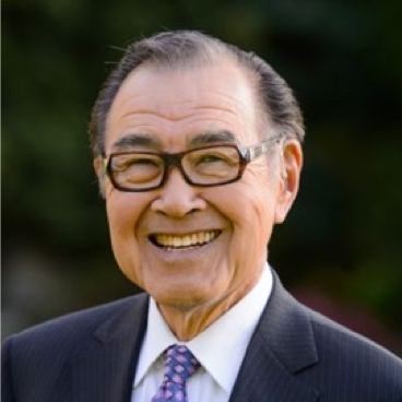 Smiling elderly man wearing glasses, a suit, and a tie outdoors