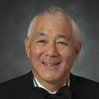 A smiling older man in a tuxedo against a gray background.