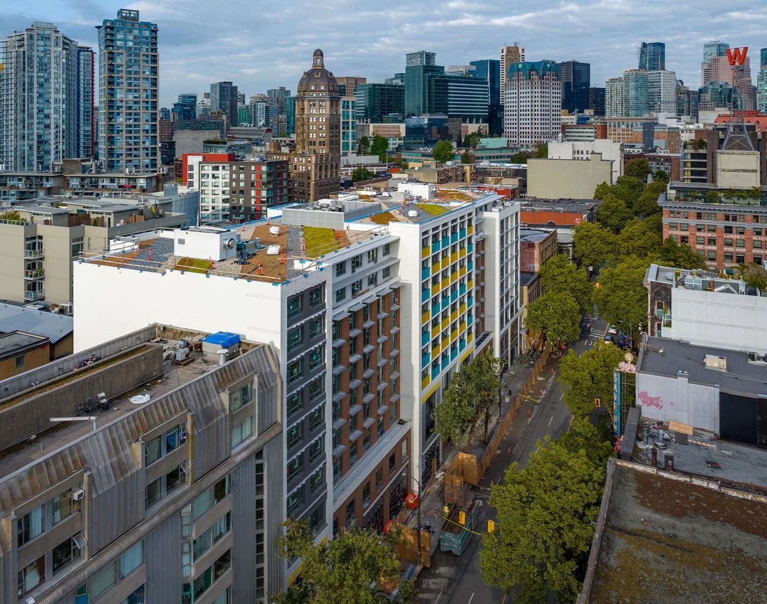 Cityscape view with high-rise buildings, green trees lining the streets, and a cloudy sky over the downtown area.