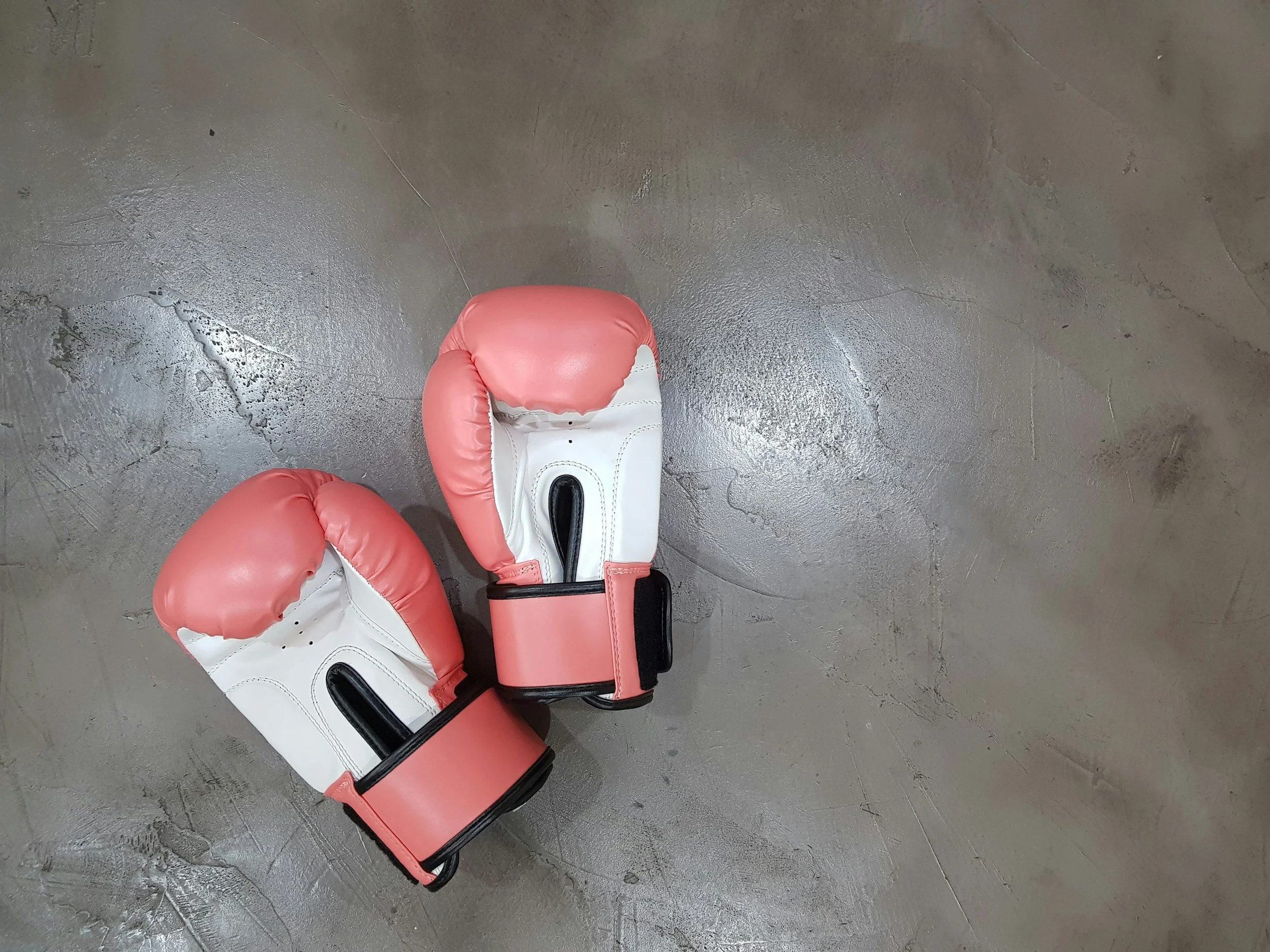 Pink and white boxing gloves resting on a concrete floor.