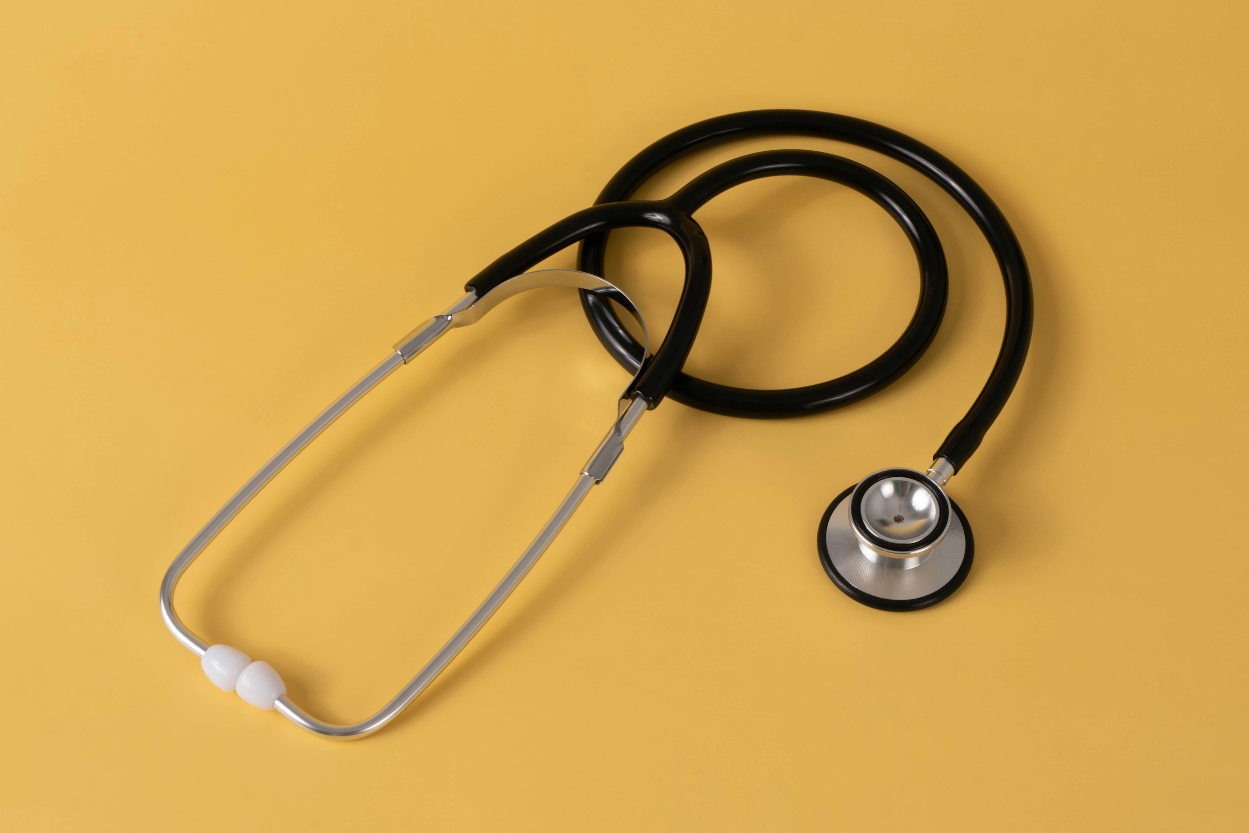 A stethoscope with black tubing and silver chest piece resting on a yellow background.
