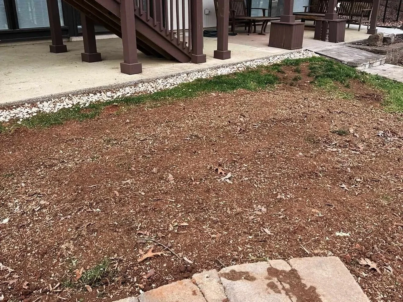 Backyard yard with a porch, stairs, some green grass, and bare dirt.