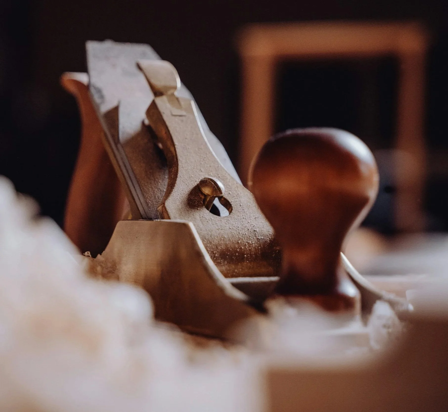 Close-up of a hand-plane showing wood shavings, slightly blurred background.