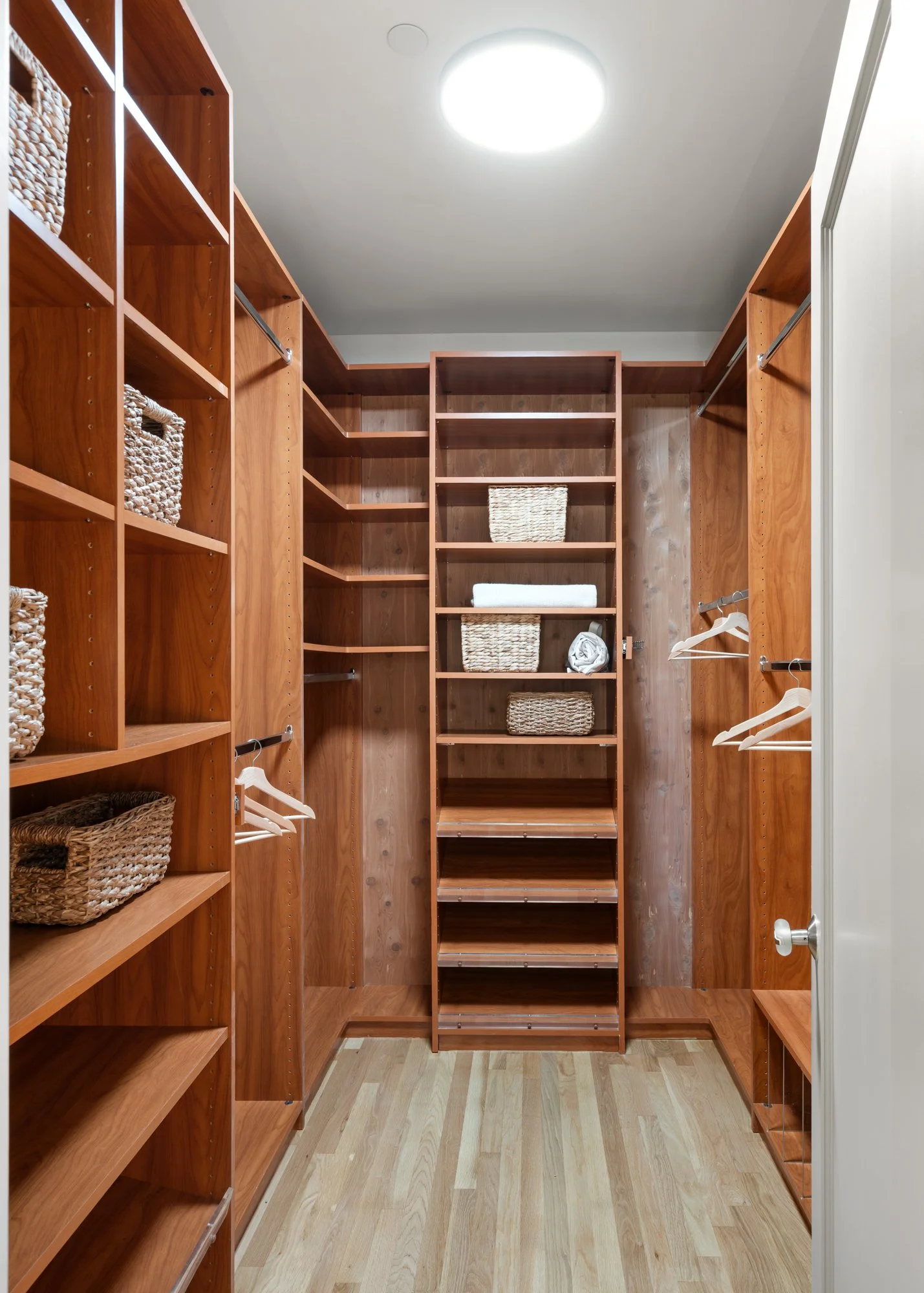Empty walk-in closet with wooden shelves, baskets, and hanging rods.