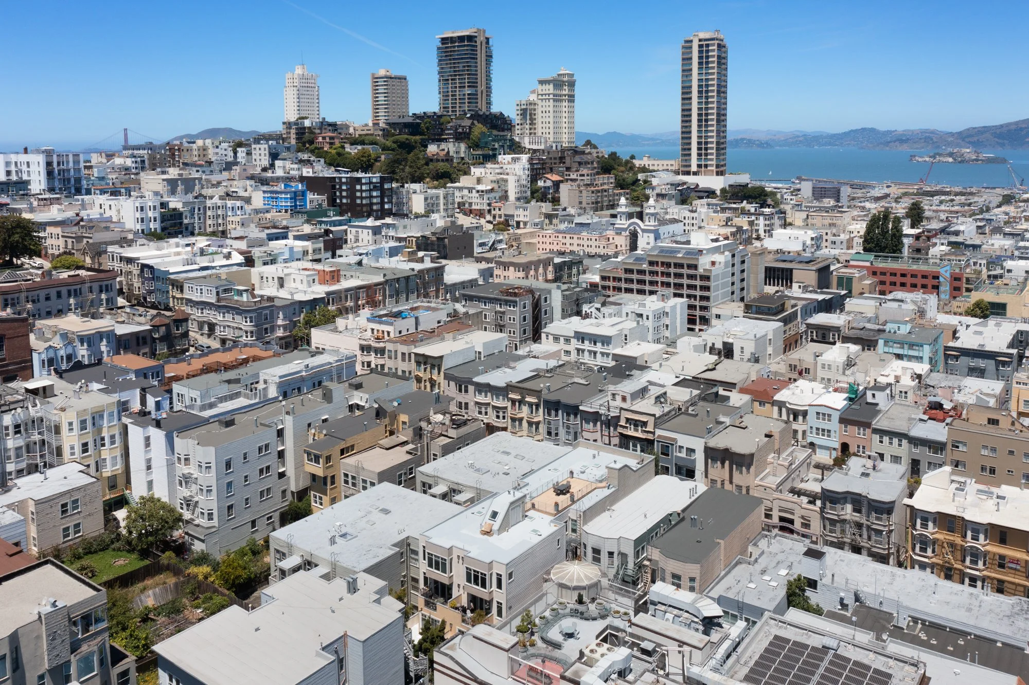 A cityscape with a dense cluster of residential buildings, some taller high-rise buildings, and a view of water and hills in the background.