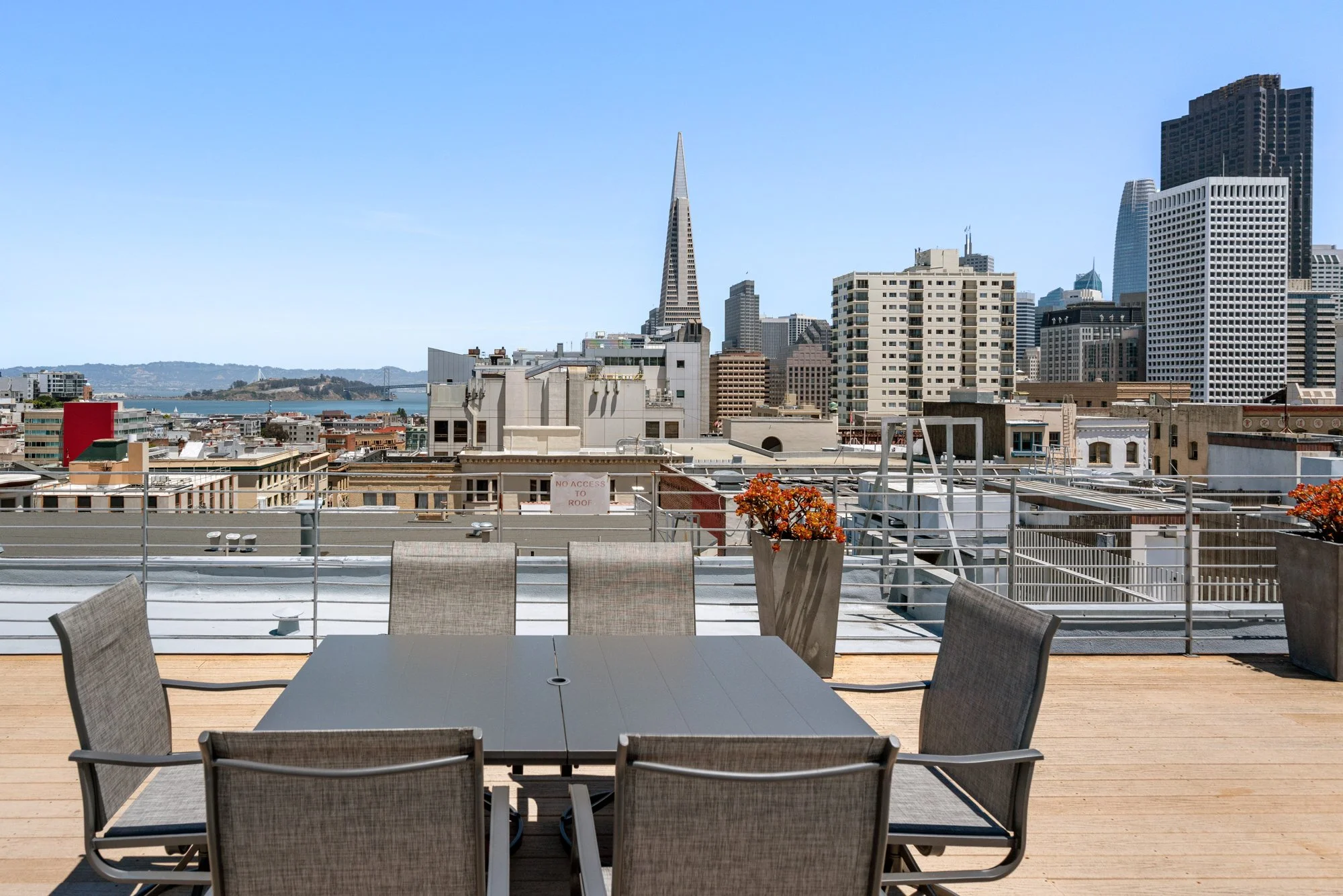 Rooftop patio with a table and chairs overlooking a city skyline, including the Transamerica Pyramid in San Francisco, with a clear blue sky.