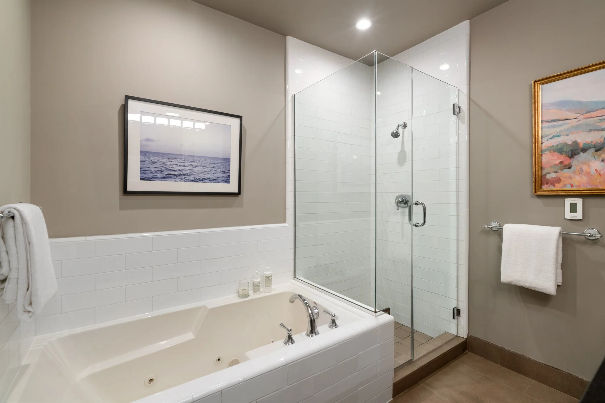 Bathroom with a bathtub, shower with glass door, and framed artwork on the walls.