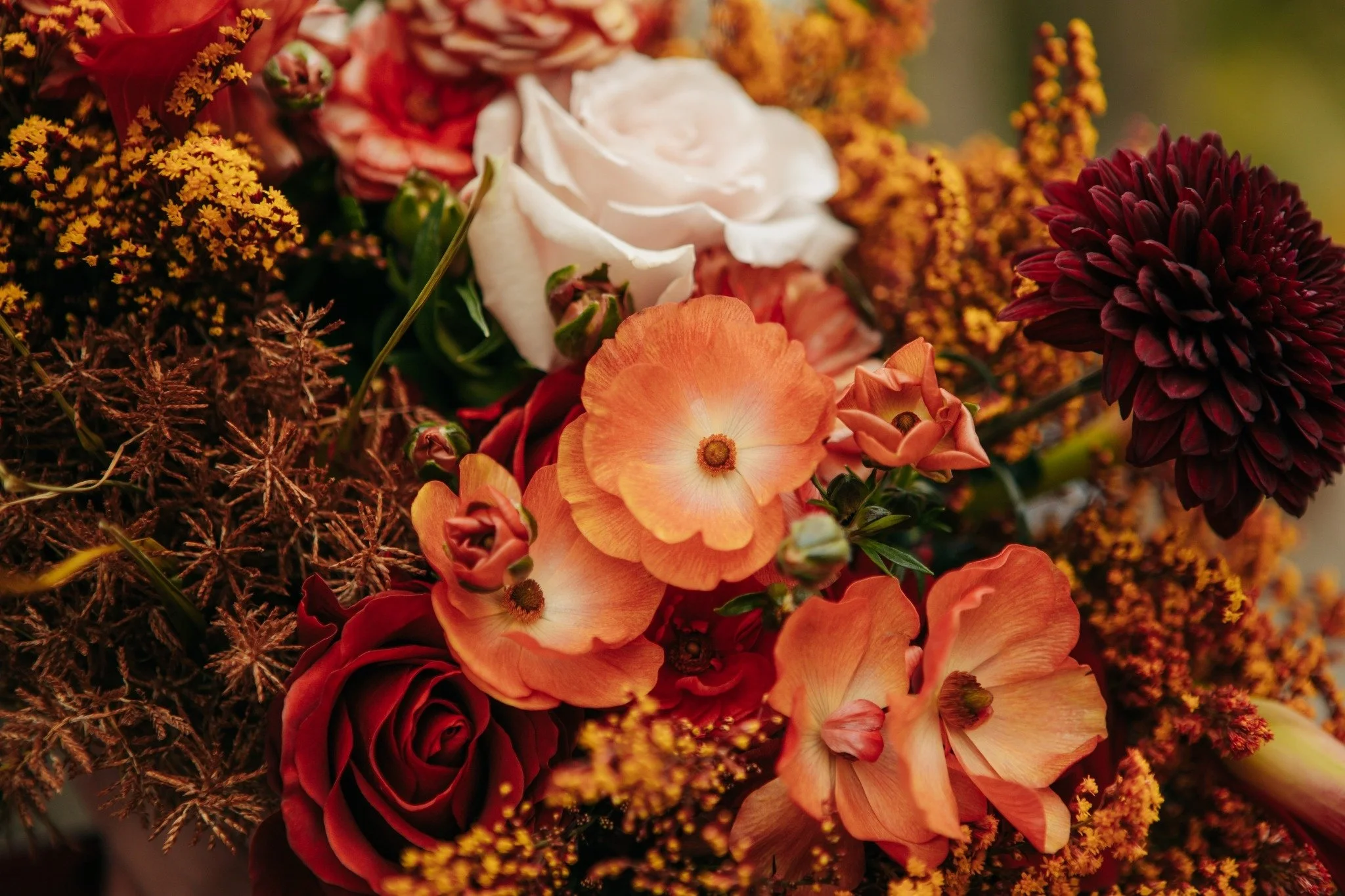 Close-up of a colorful flower bouquet with white and orange roses, red chrysanthemums, and yellow and orange small flowers.