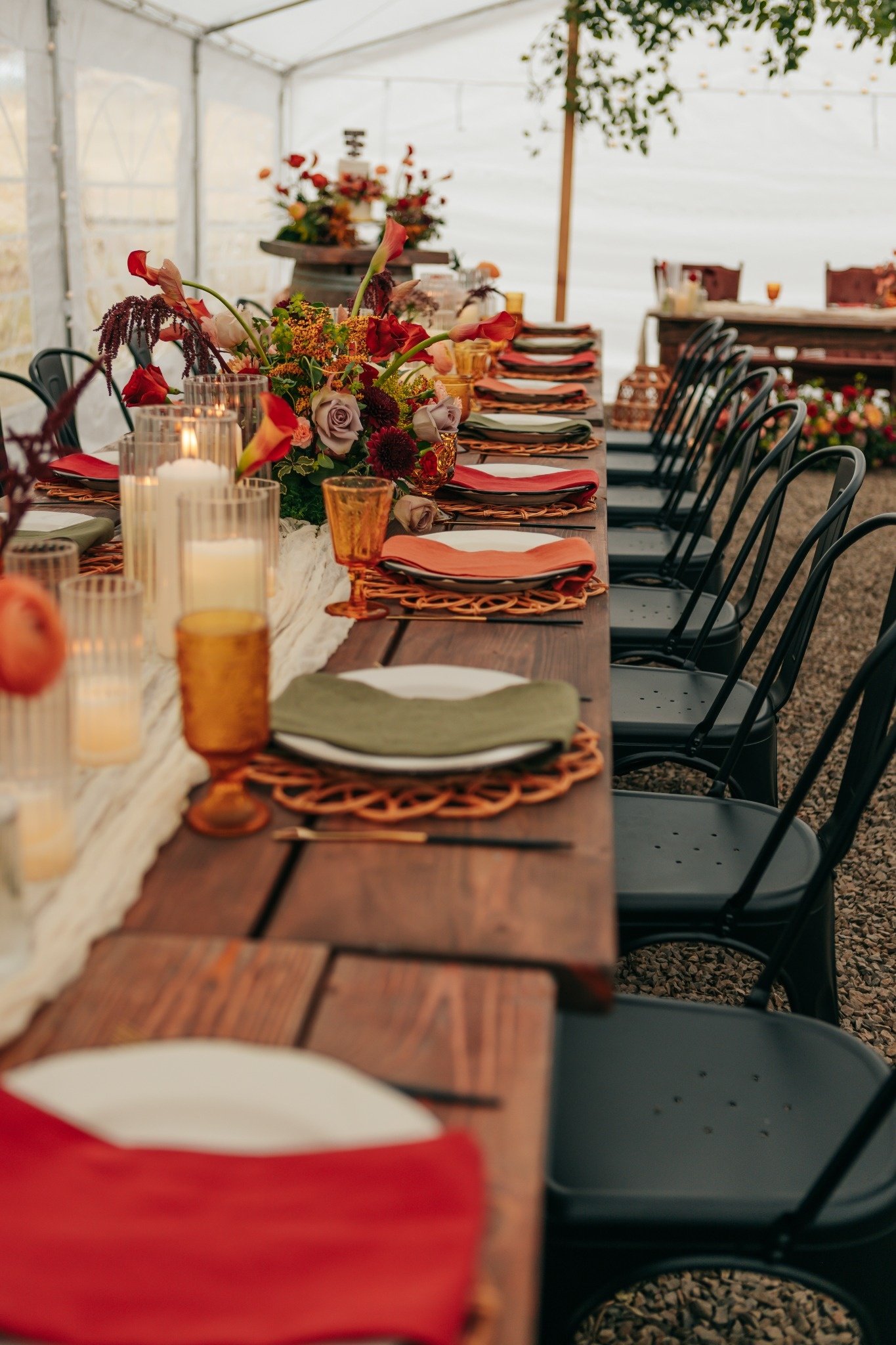 A long dining table set up inside a tent with floral centerpieces, candles, and place settings, likely for a celebration or event, with chairs along each side.