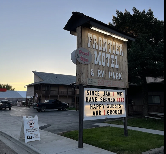 Signboard for Frontier Motel & RV Park with a message board counting guests and greeting guests, next to a parking lot and building with cars parked.