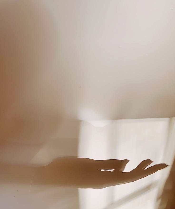 Shadow of a person's hand on a plain, light-colored wall with sunlight streaming through window.